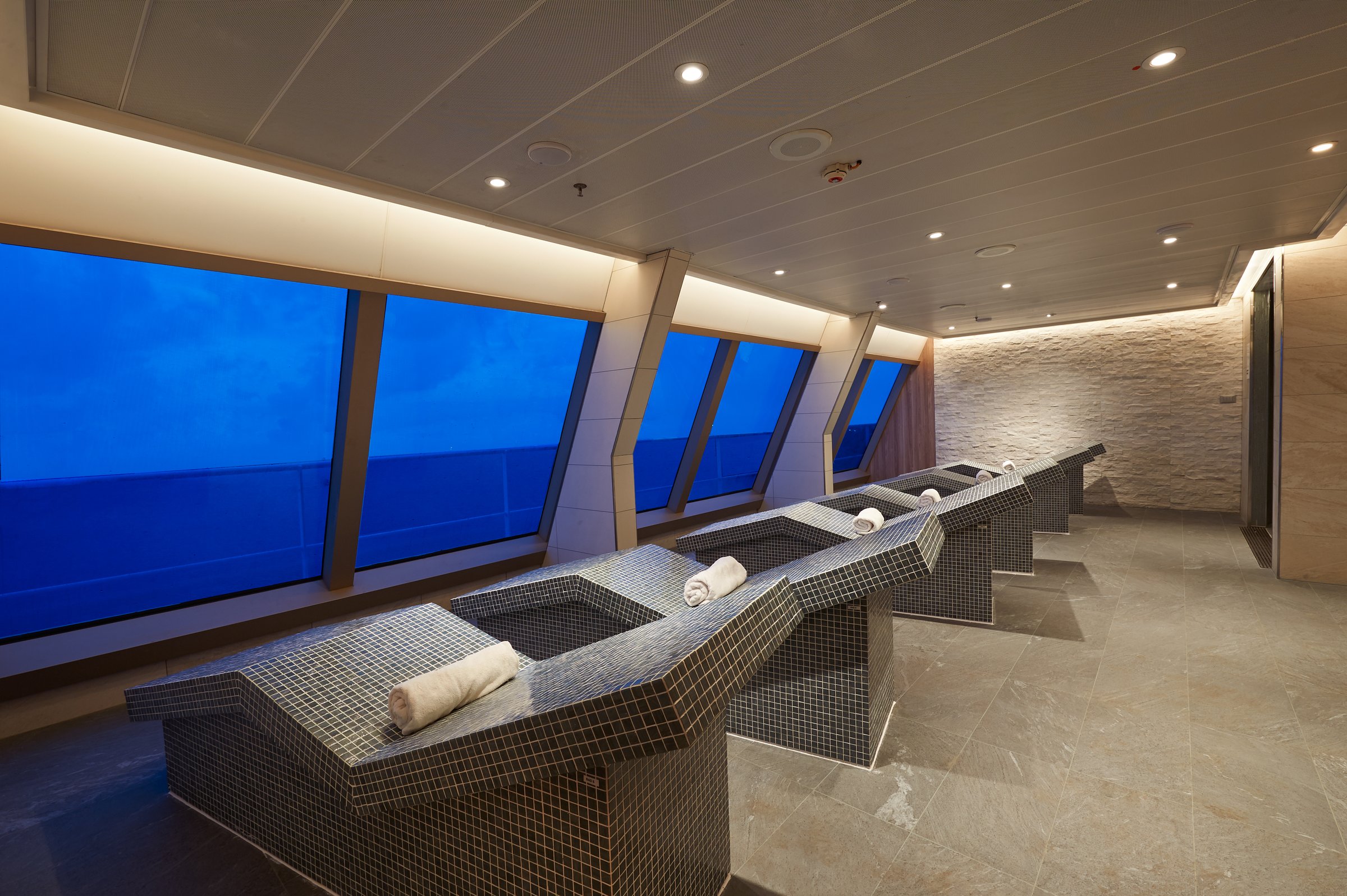 Carnival Sunrise Cloud 9 Spa thermal suite with tiled heated loungers facing floor-to-ceiling ocean windows