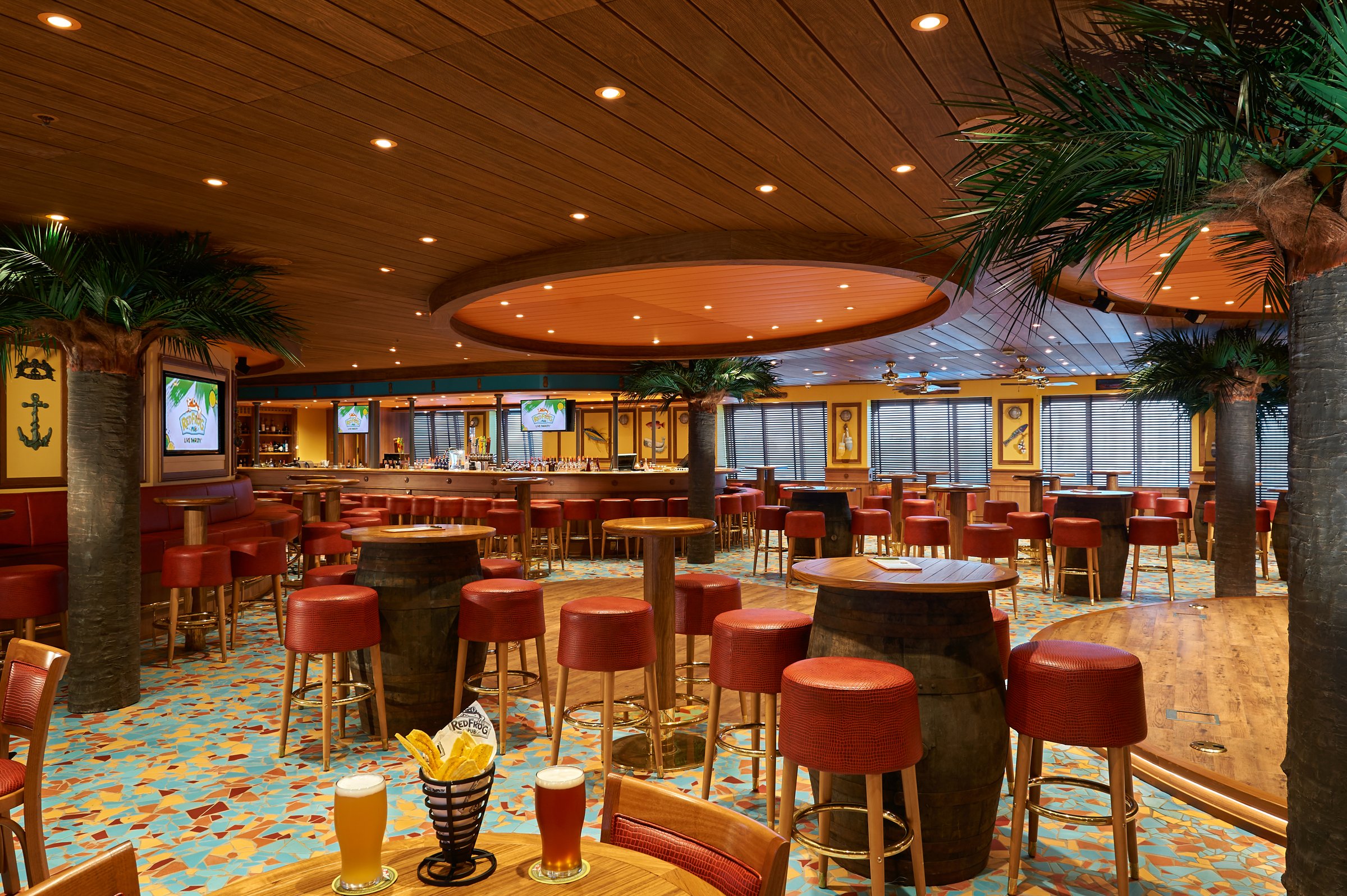 Carnival Sunrise RedFrog Pub with barrel tables, red stools, palm trees and a colourful tiled floor