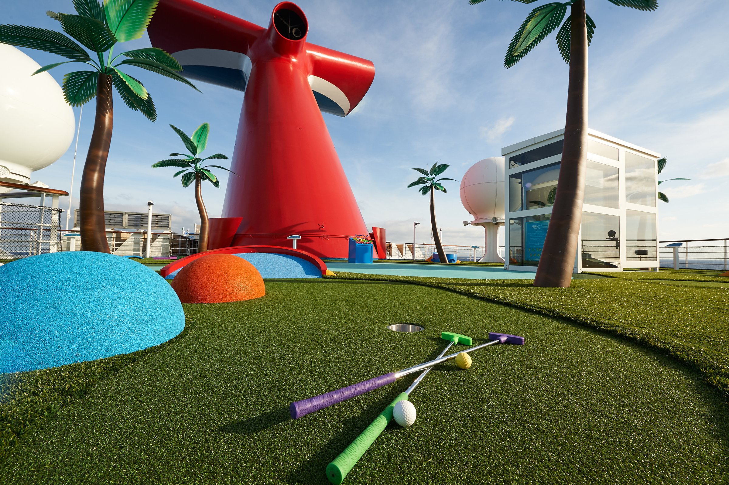Carnival Sunrise mini golf course with putters, a ball and the red funnel among palm trees
