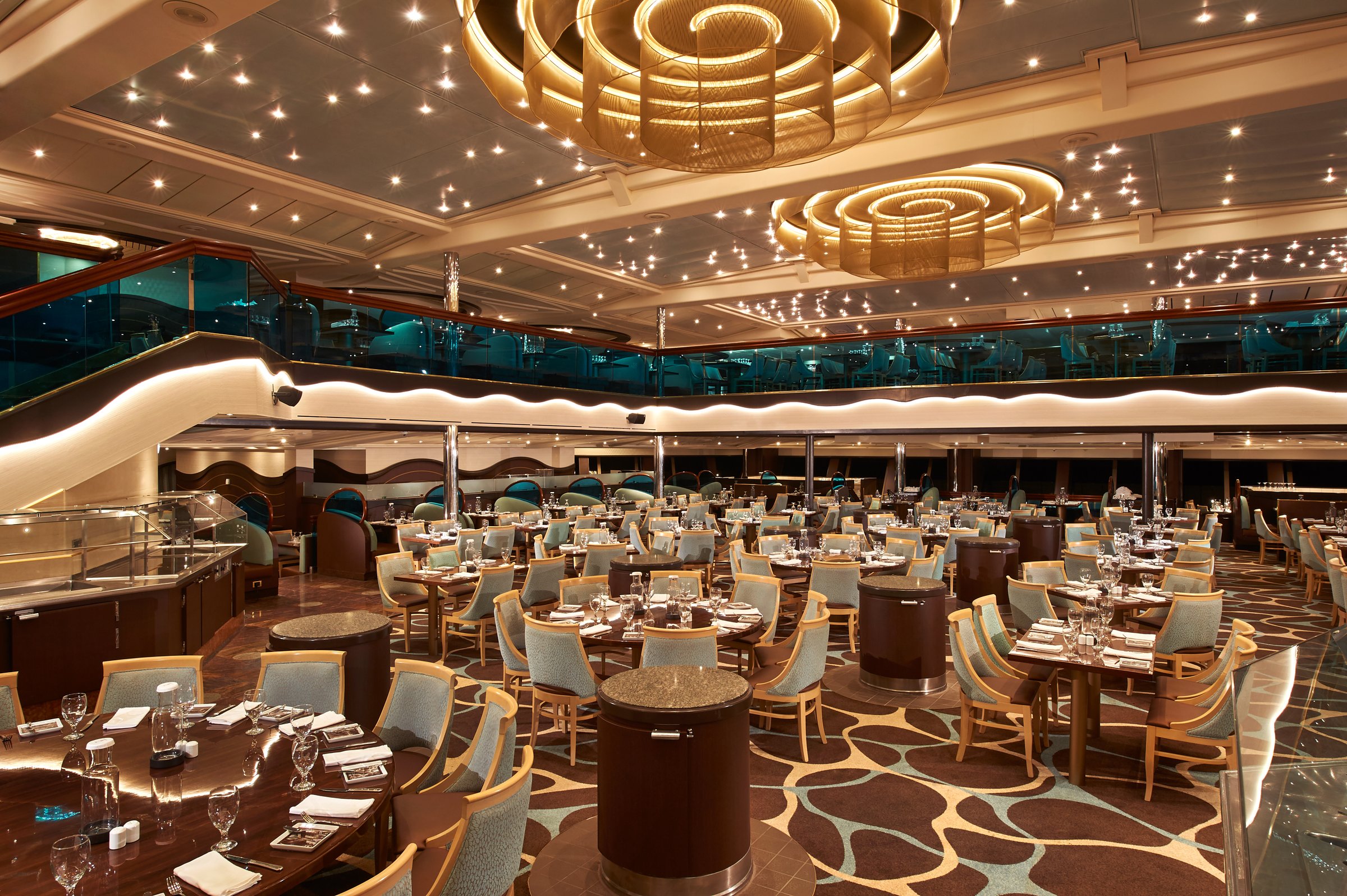 Carnival Sunrise main dining room with gold swirl chandeliers, round tables and a patterned floor