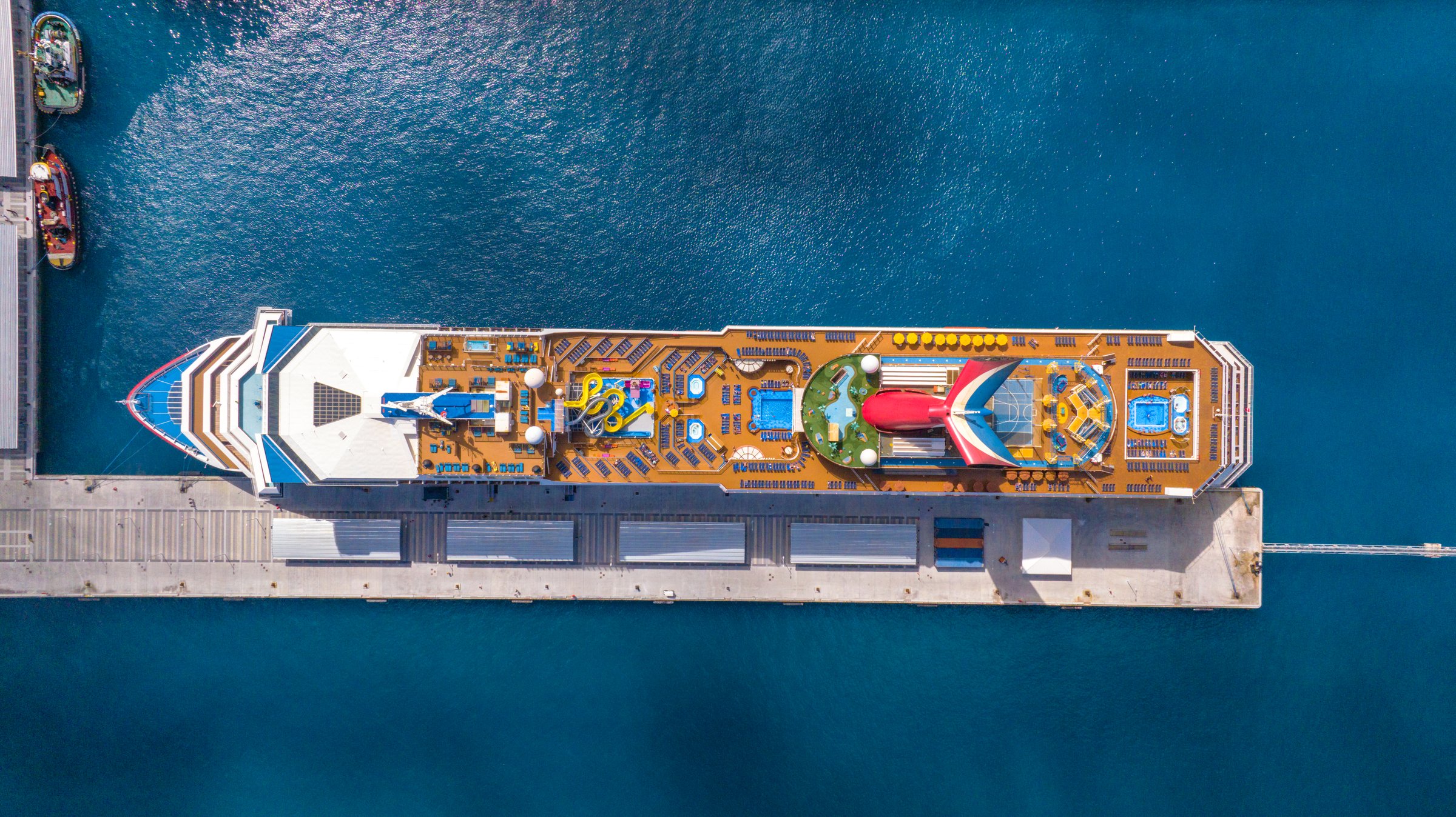 Carnival Sunrise seen from directly above alongside a pier in deep blue water