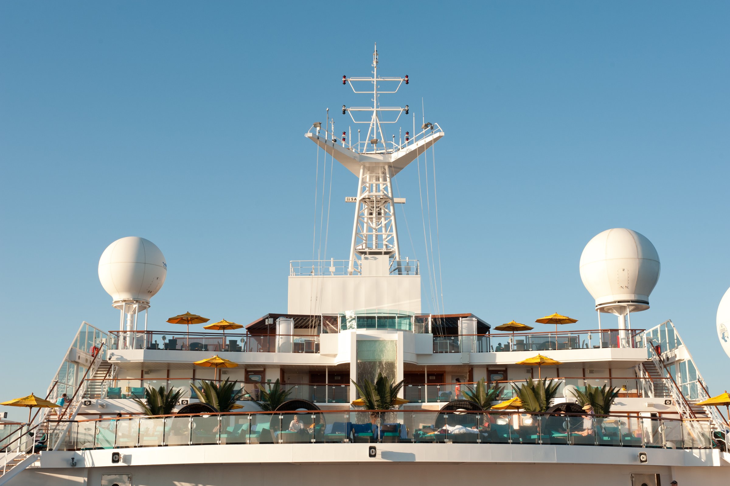 Carnival Sunshine upper decks with radar domes, mast and umbrellas against a clear blue sky