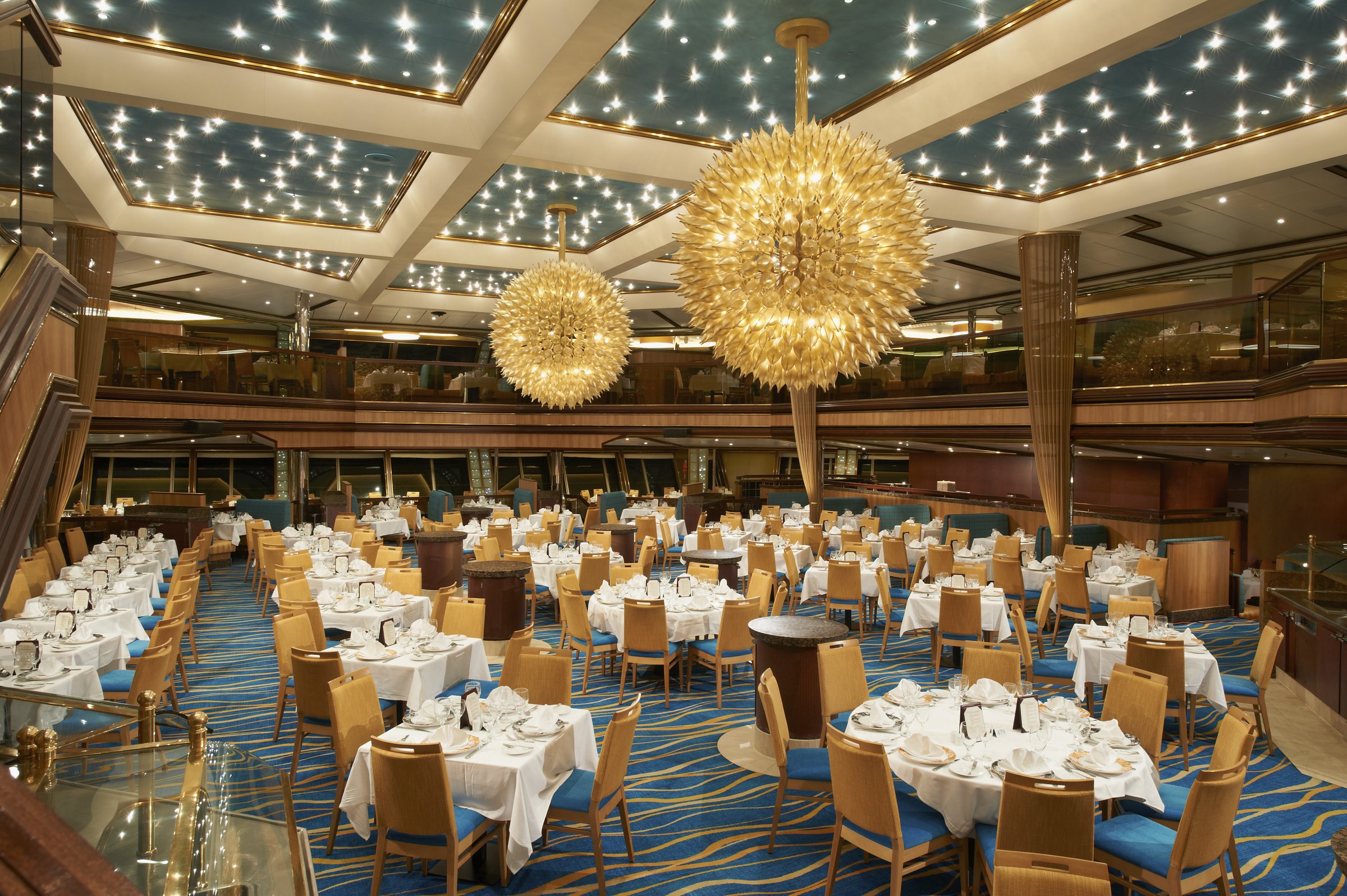 Carnival Sunshine main dining room with starburst chandeliers, white-clothed tables and blue carpet