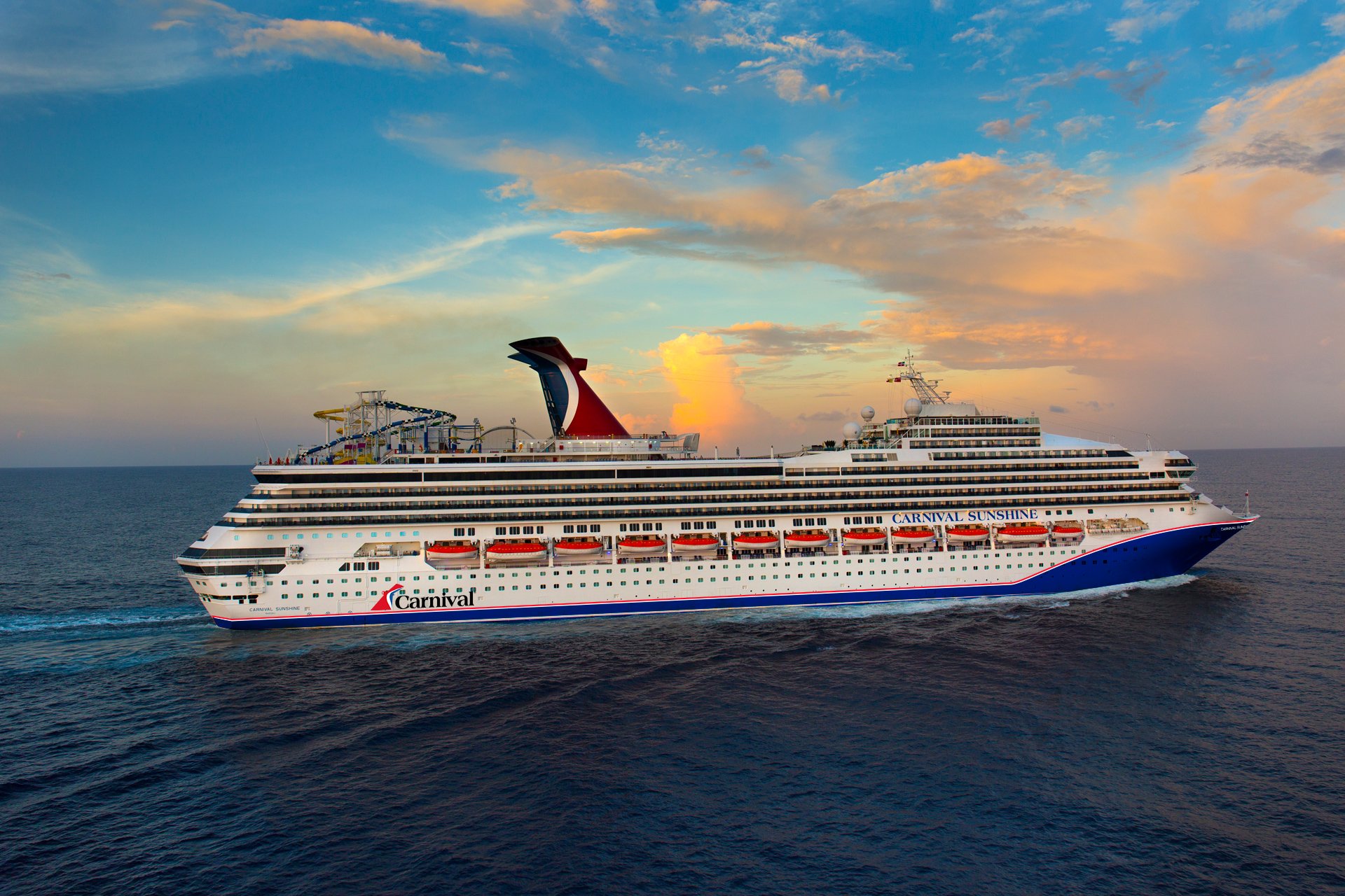 Carnival Sunshine at sea under a colourful sunset sky, side view of the hull and funnel