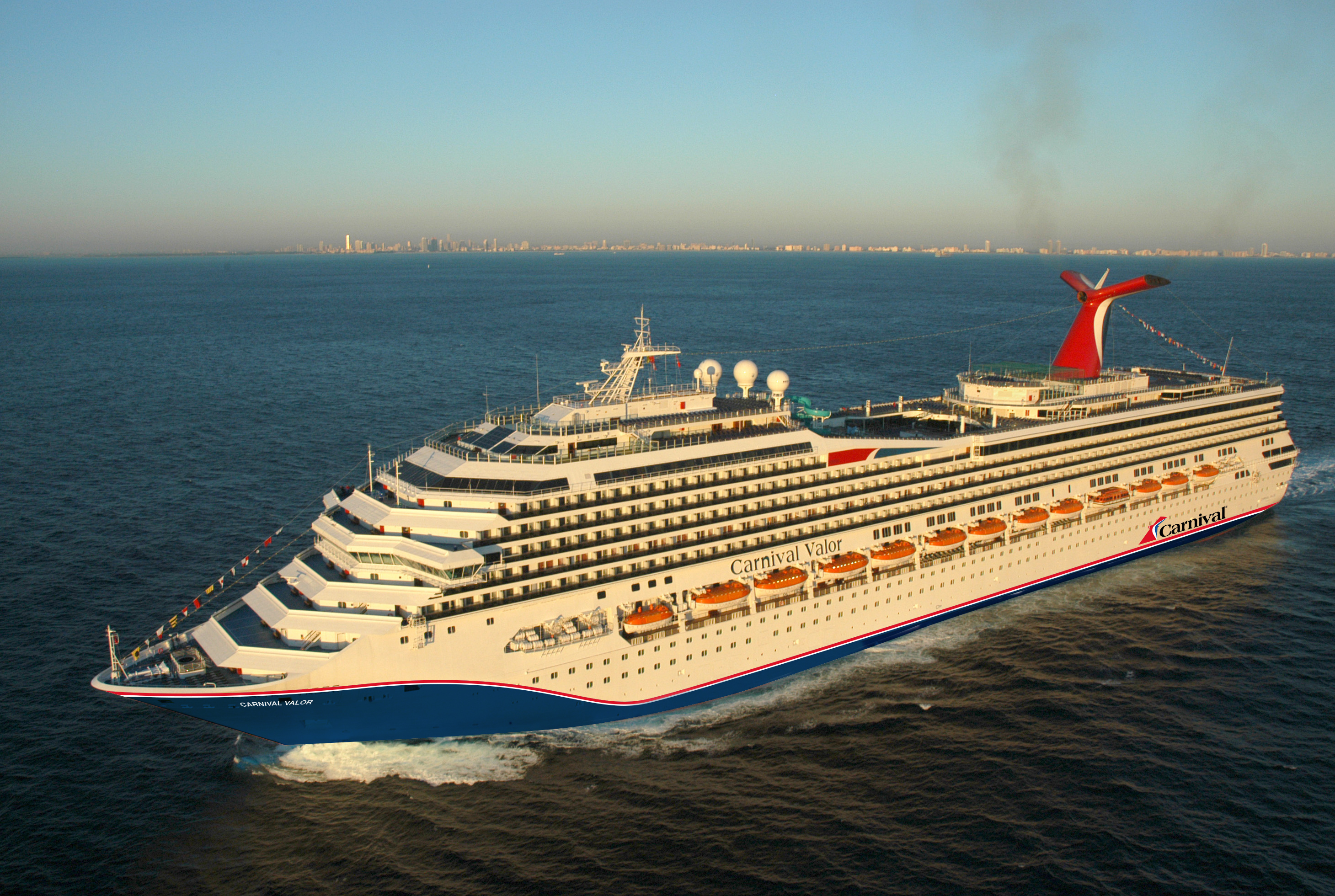 Carnival Valor blue hull aerial underway with city skyline on the horizon