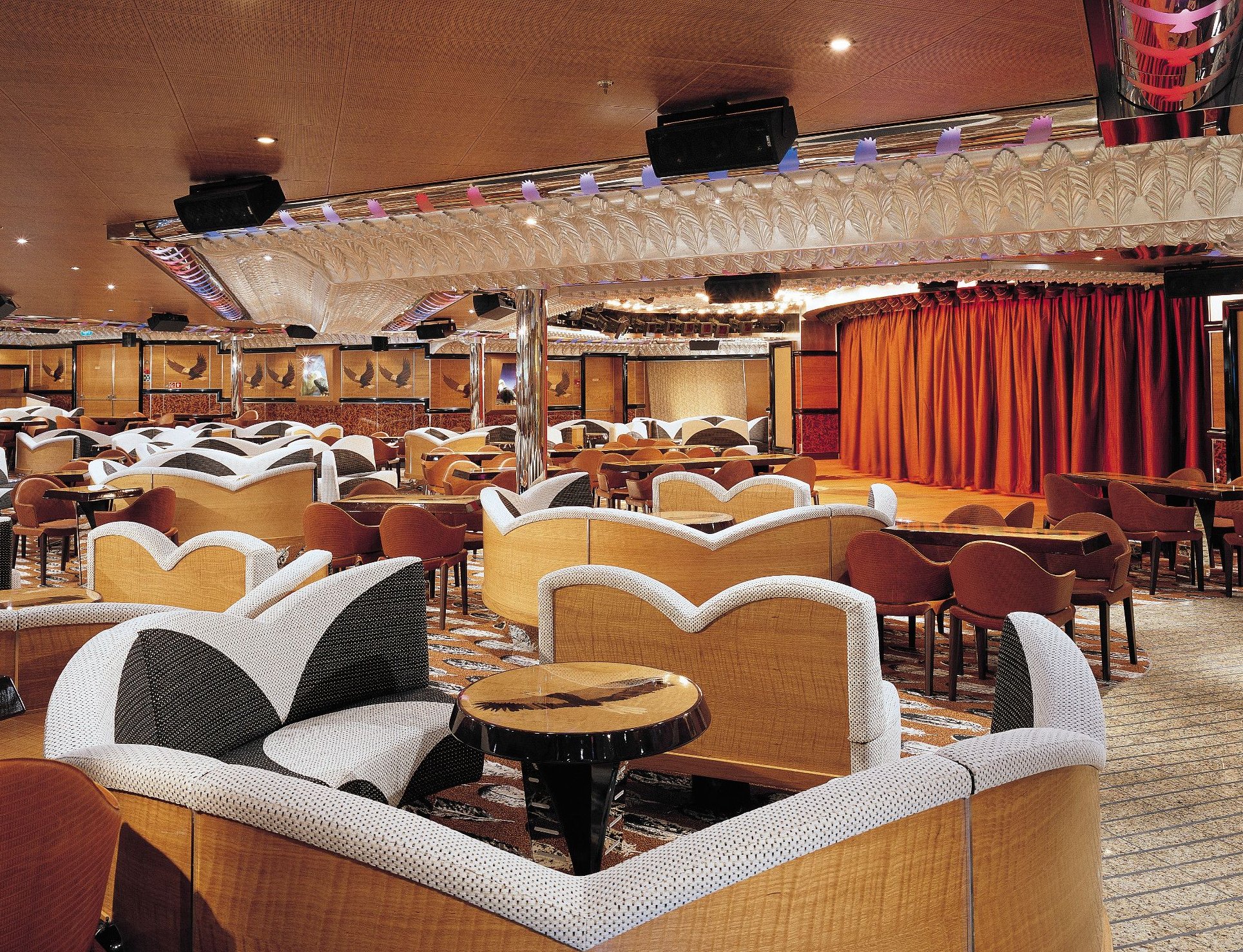 Carnival Valor public lounge with curved banquettes, dance floor and a stage with orange curtain