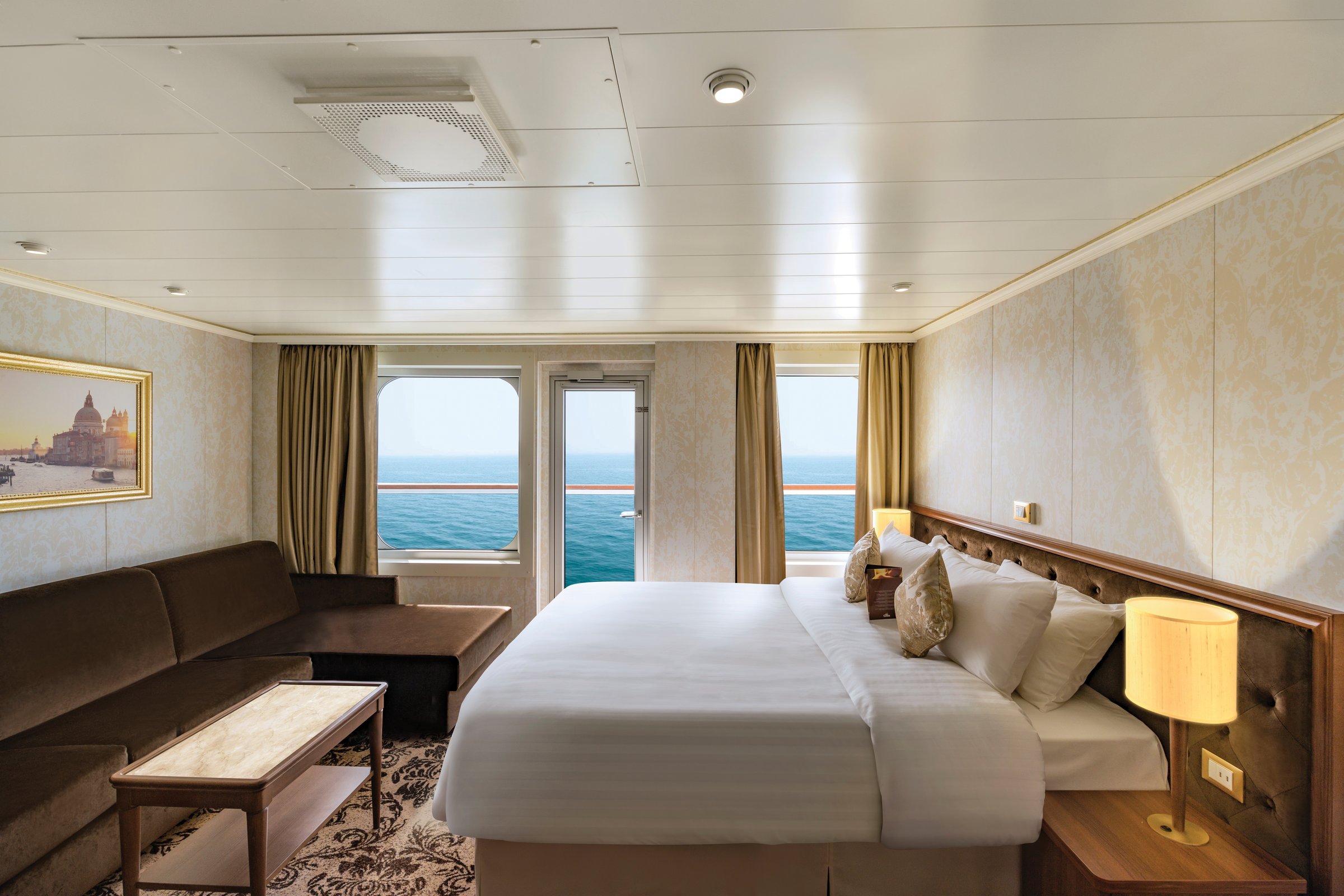 Carnival Venezia balcony suite with a king bed, sofa lounge and sea-view balcony doors