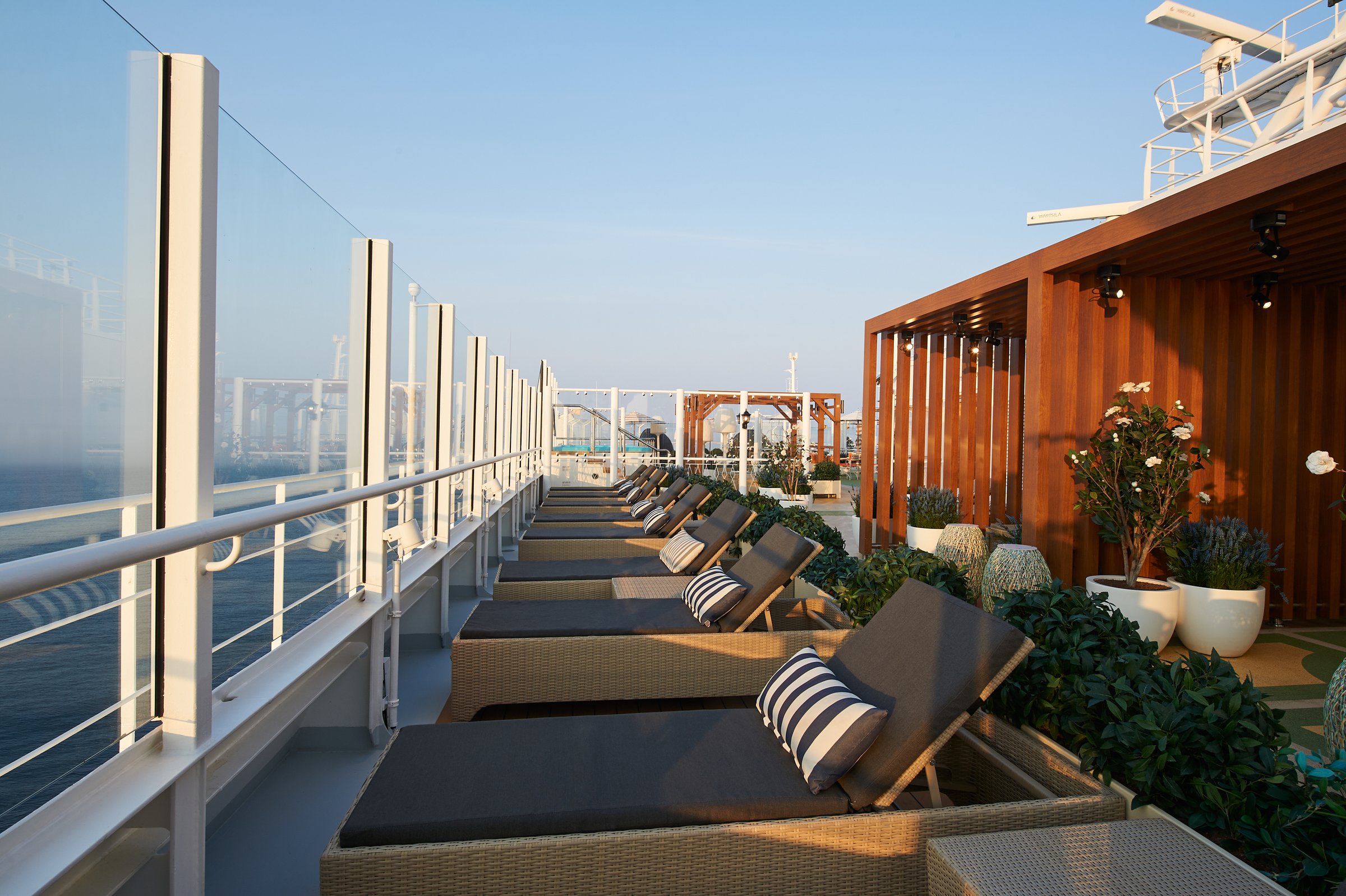 Carnival Venezia Serenity retreat loungers lined along the glass rail with planters and cabanas