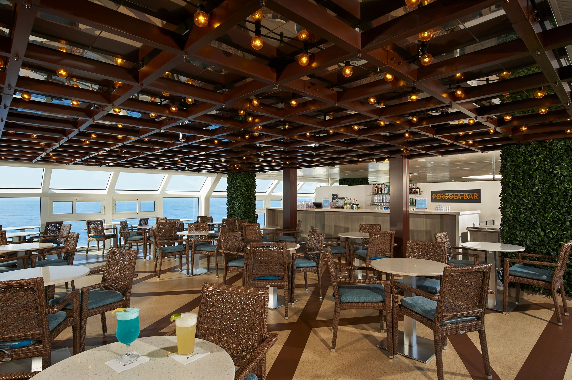 Carnival Venezia Pergola Bar with wicker chairs, a lantern-lit wooden ceiling and ocean windows