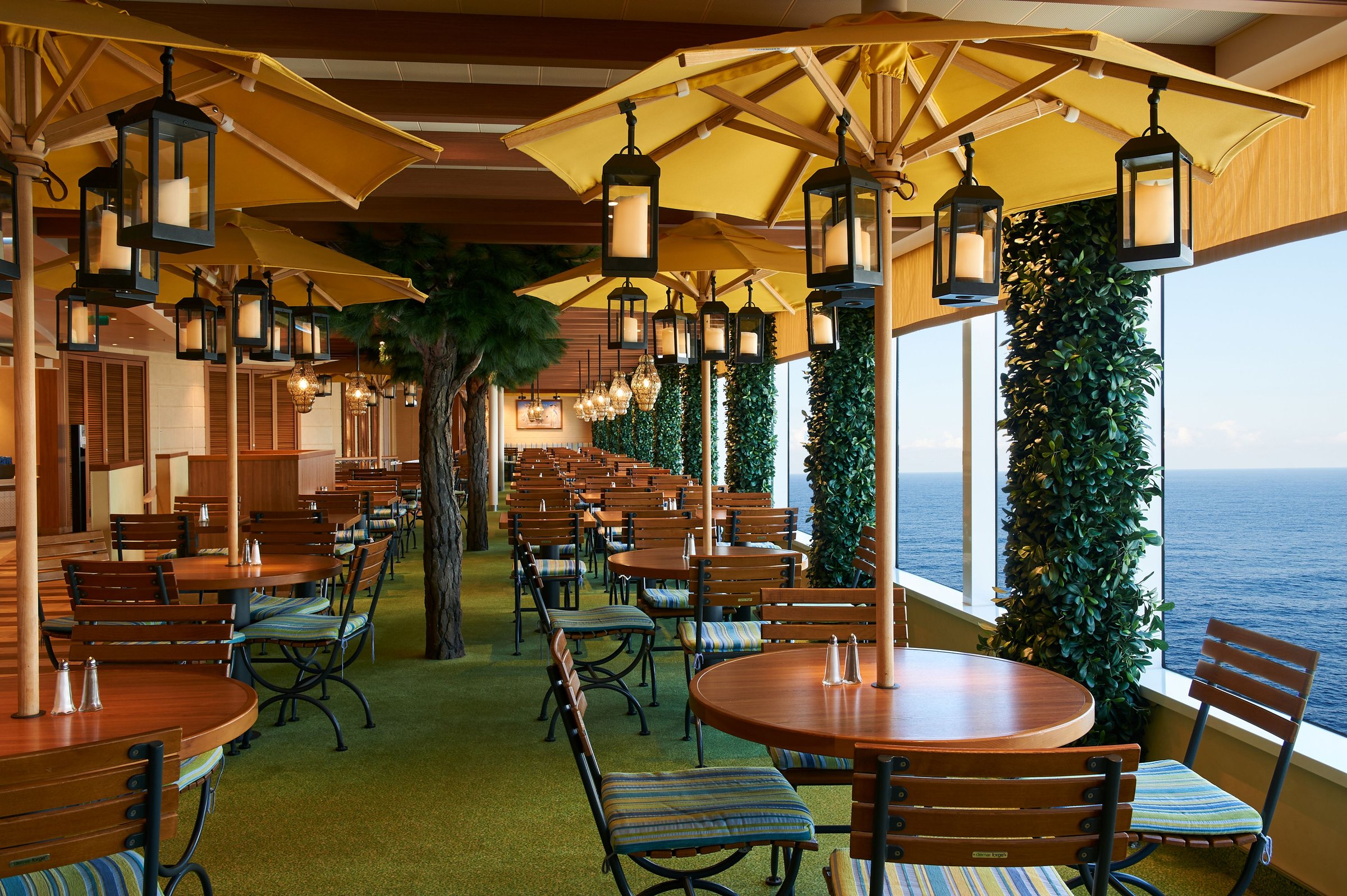 Carnival Venezia Lido Marketplace terrace seating under yellow umbrellas and lanterns beside the sea