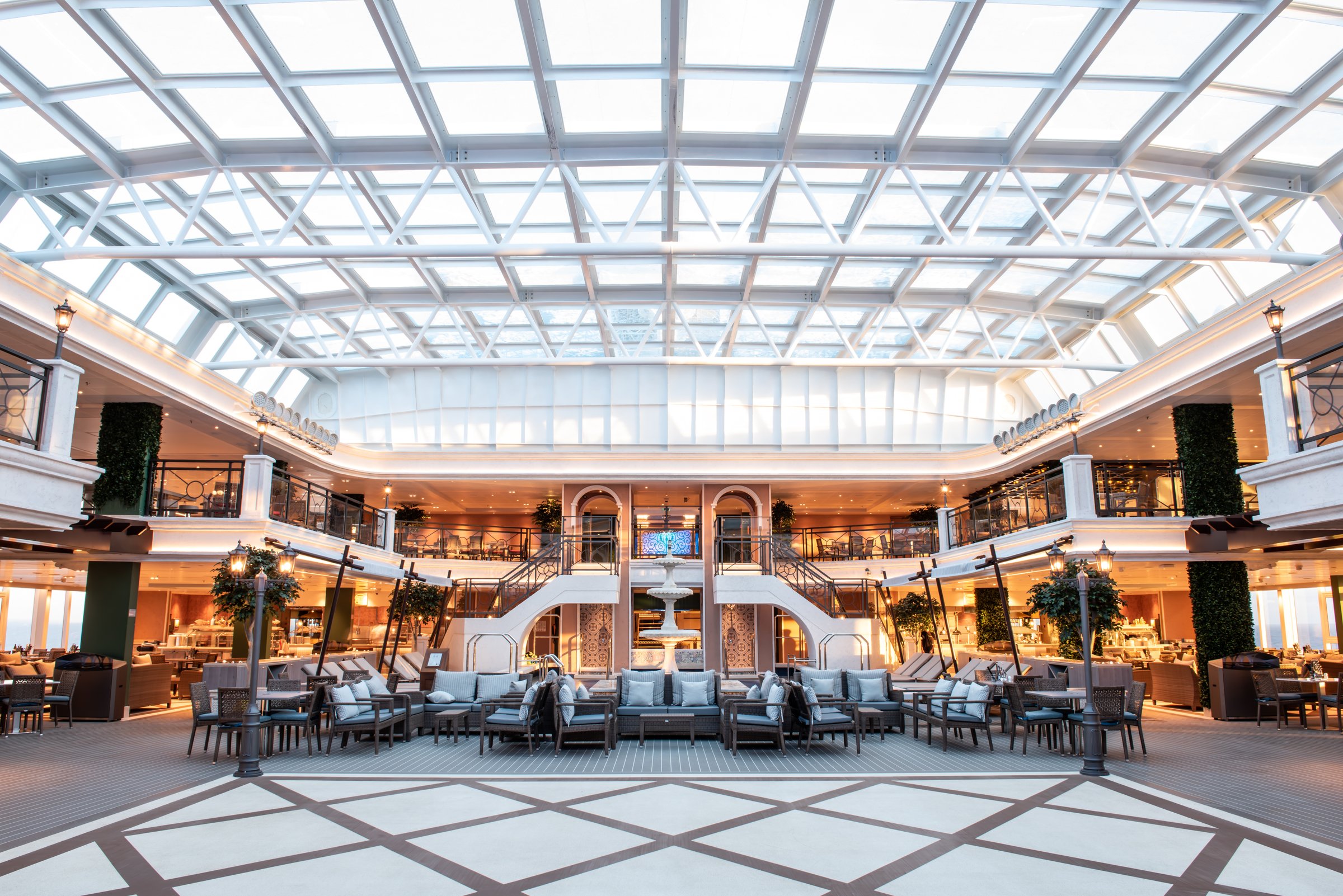 Carnival Venezia glass-roofed covered pool area lounge with sofas, a fountain and sweeping stairways