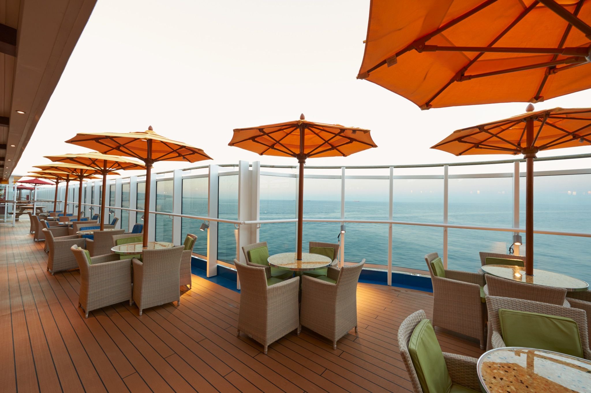 Carnival Vista Lanai promenade with wicker seating under orange umbrellas along the sea rail