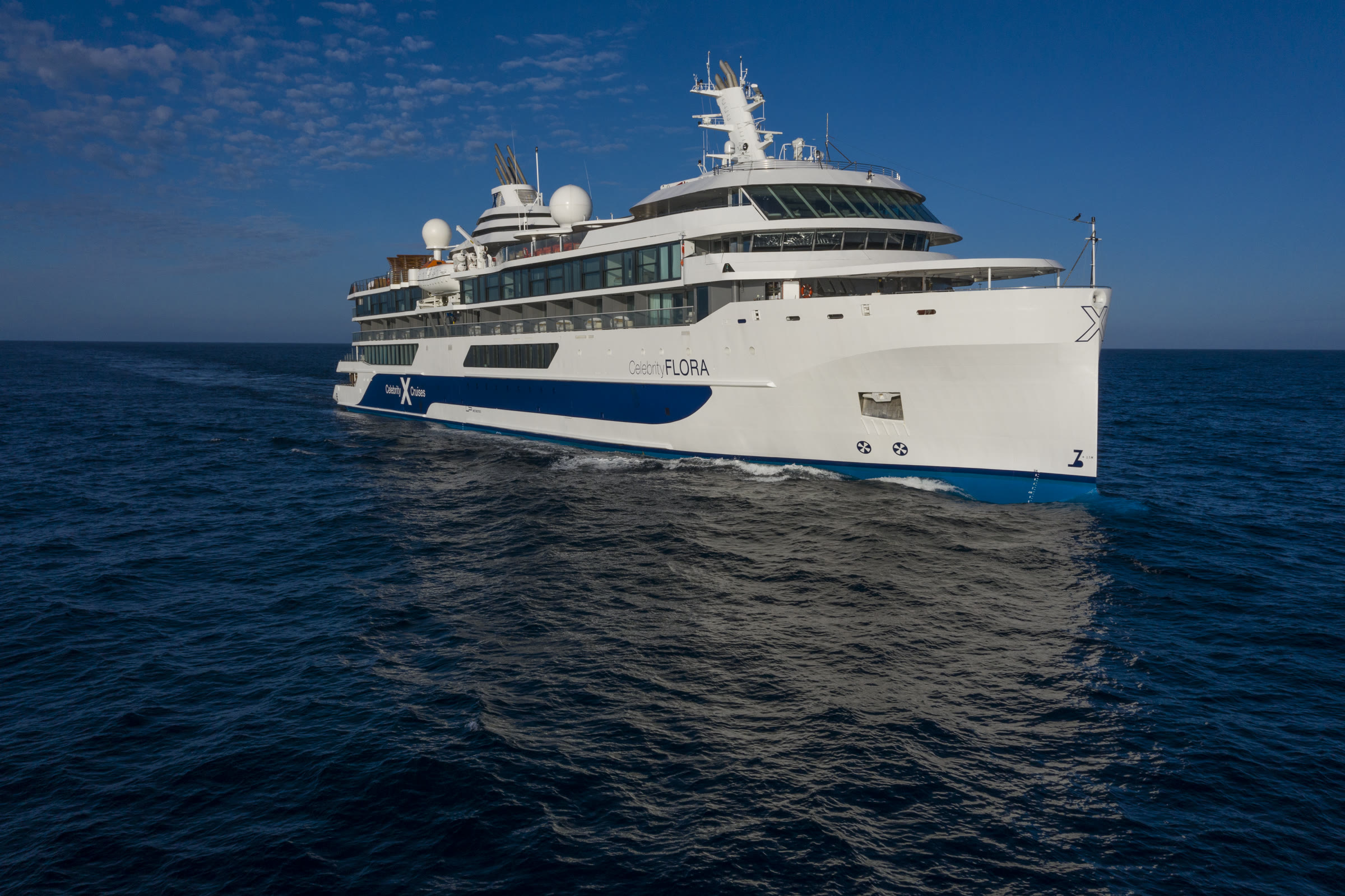 Celebrity Flora sailing under blue sky, full-ship profile over open ocean