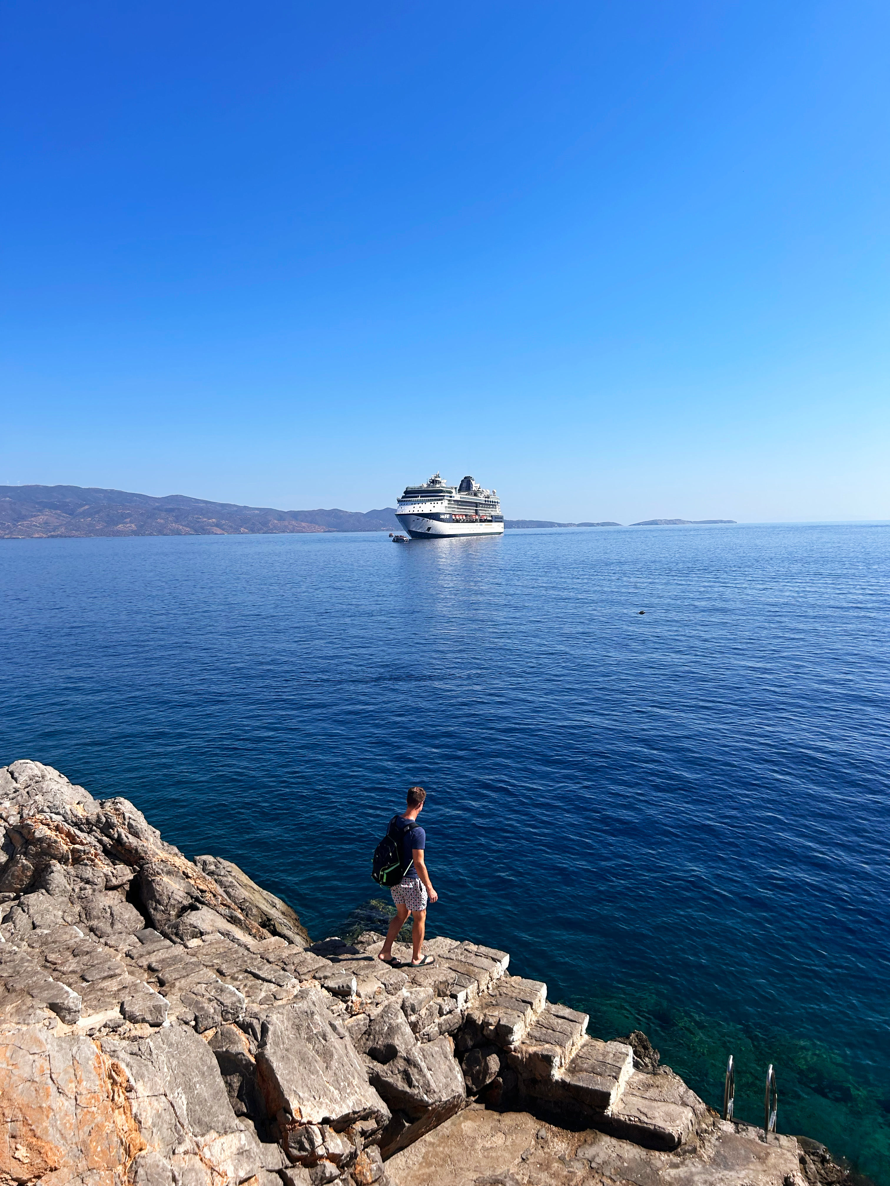 Celebrity Infinity at anchor off a sunny rocky shore