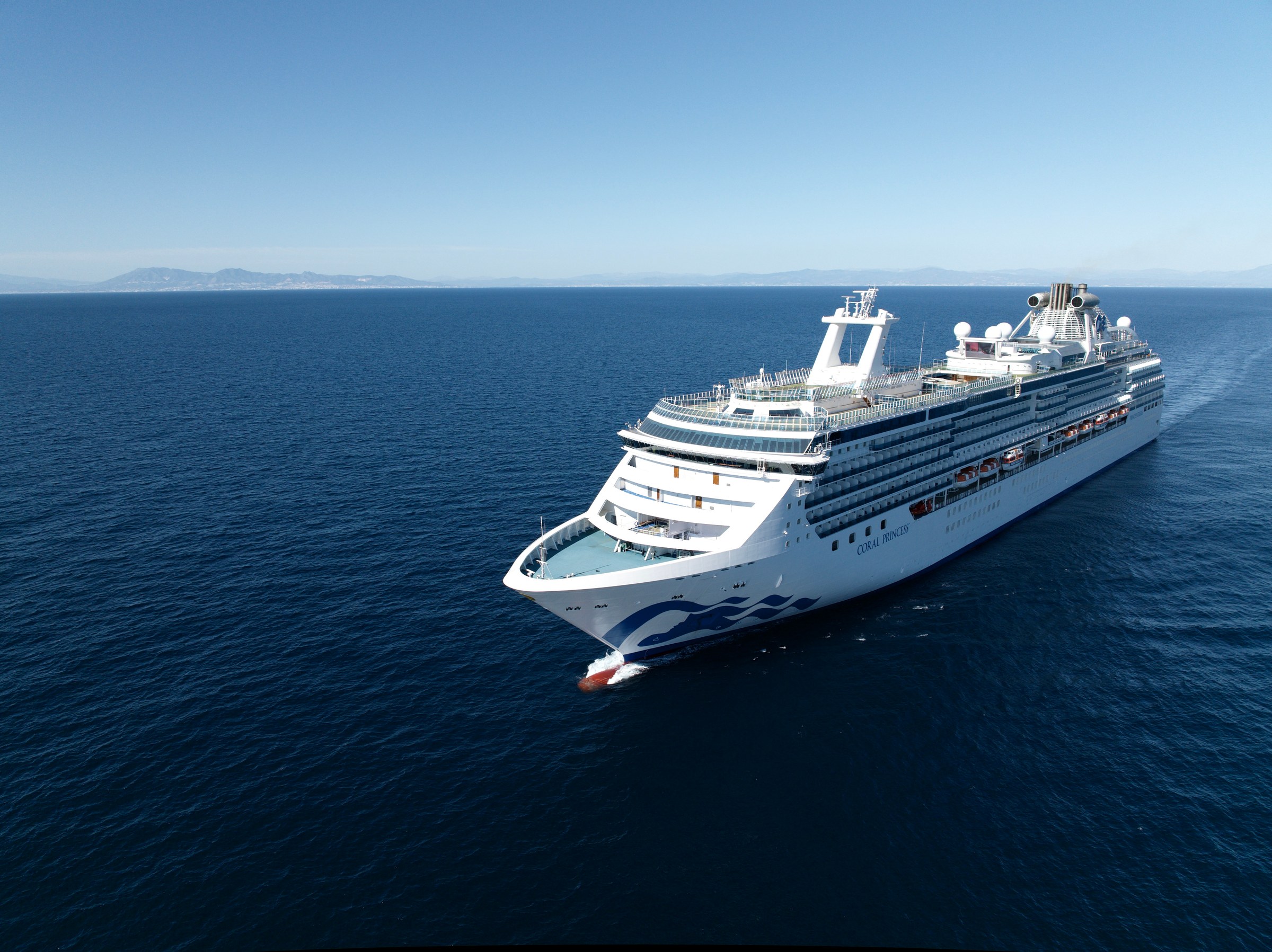 Aerial of Coral Princess sailing calm blue water near a distant coastline