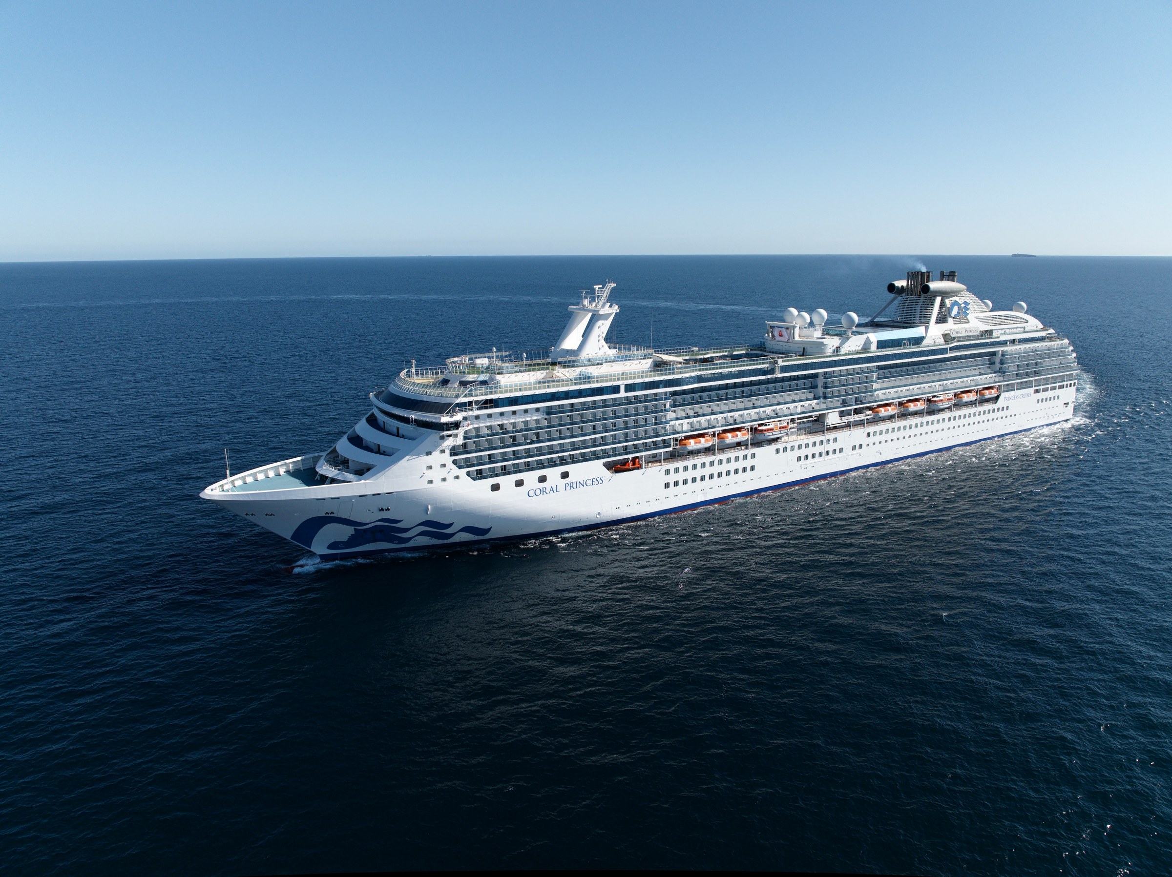 Coral Princess side profile in a clear blue ocean from the air