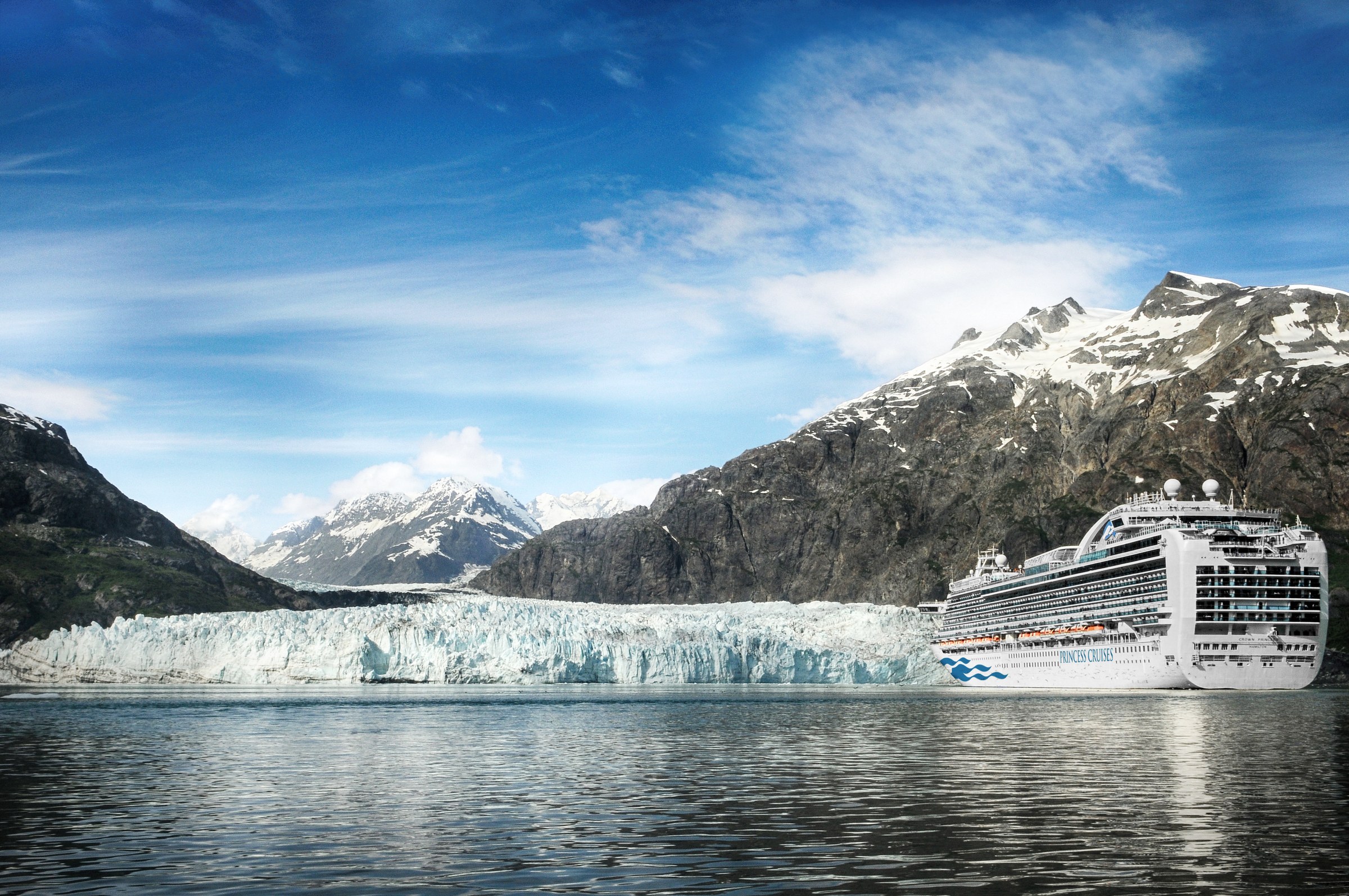 Crown Princess beside a tidewater glacier and snowy peaks in Glacier Bay, Alaska