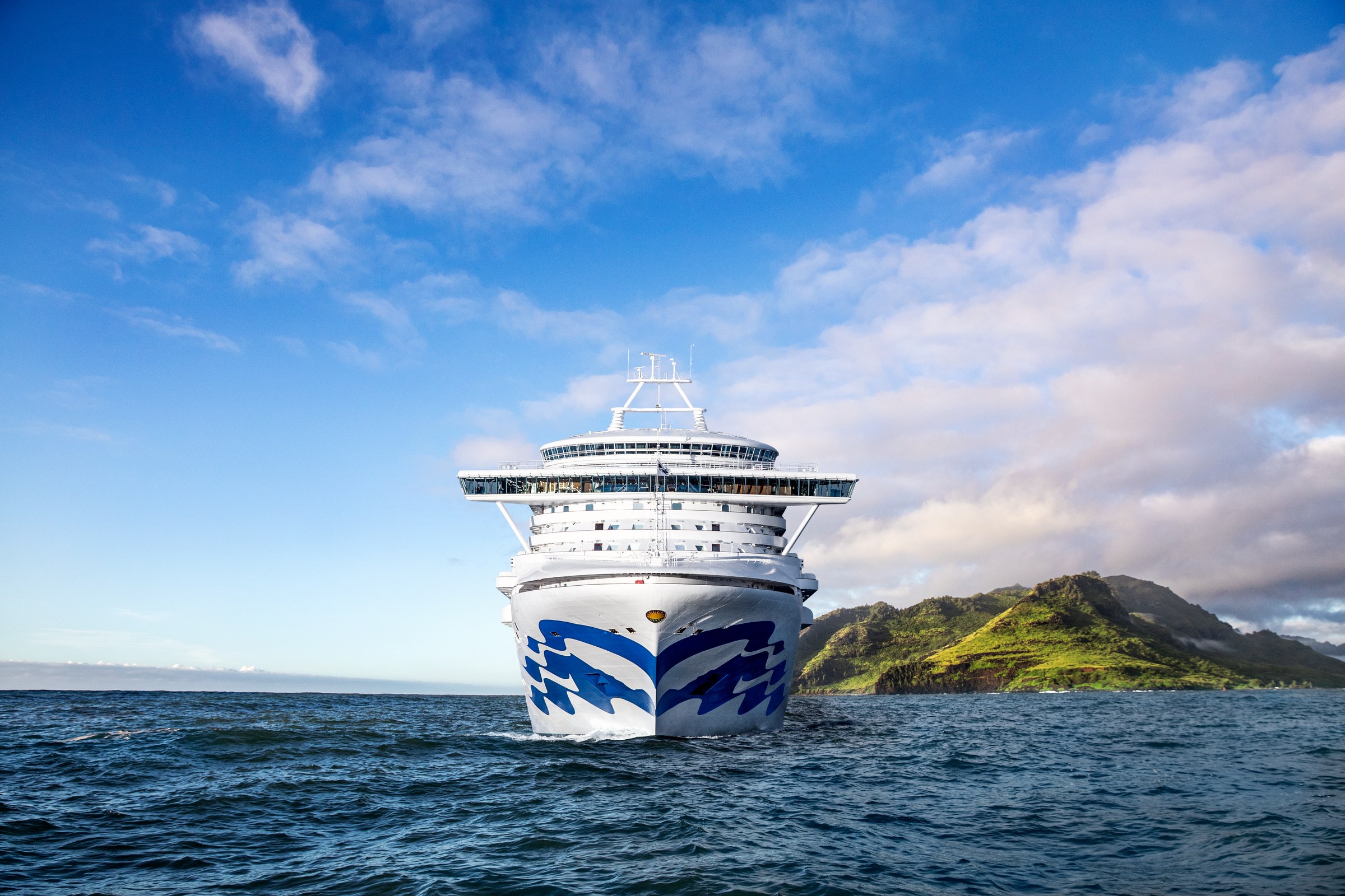Grand Princess bow sailing toward a lush green Hawaiian island under blue sky