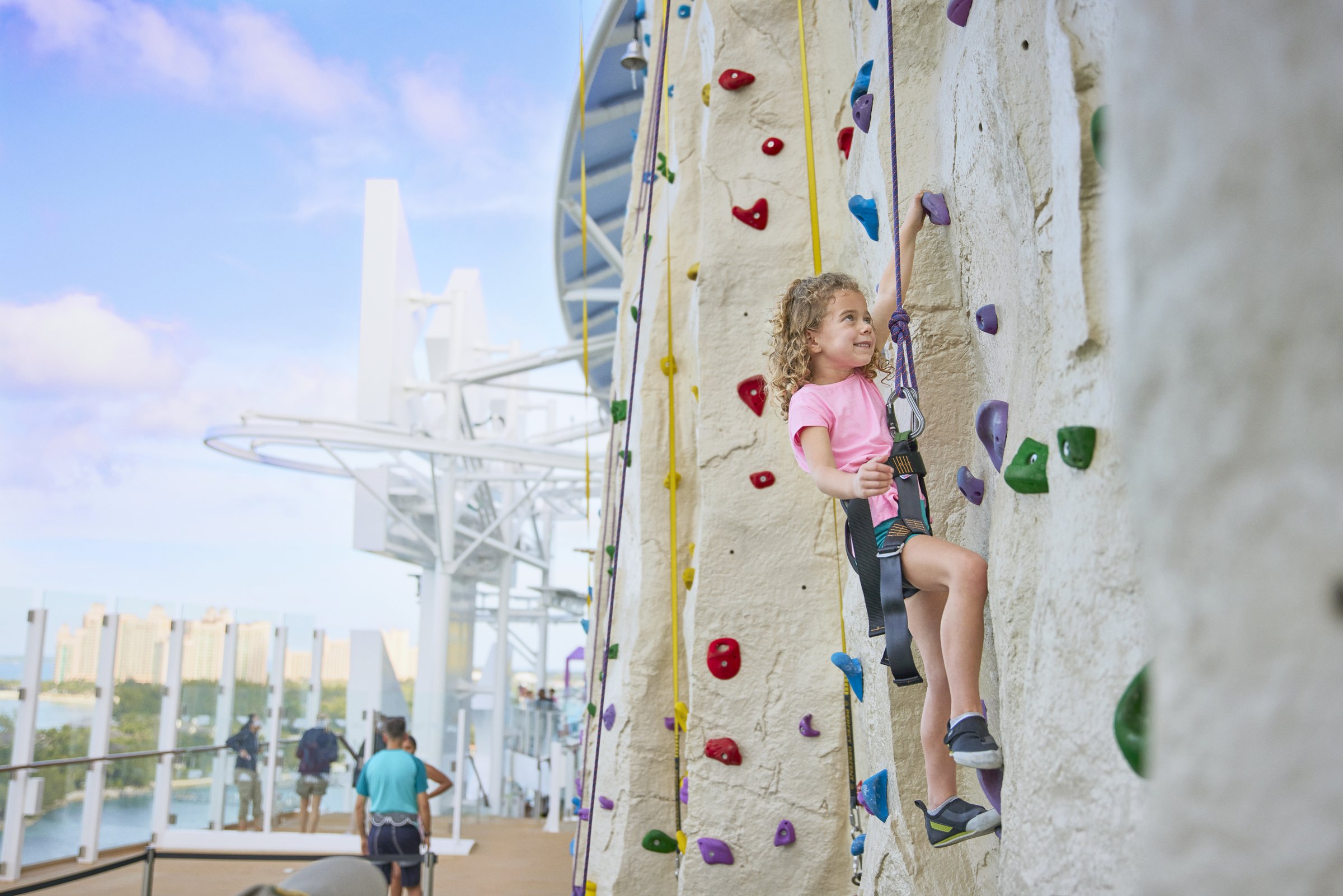 Young climber on the Adrenaline Peak rock wall aboard Icon of the Seas on a bright day