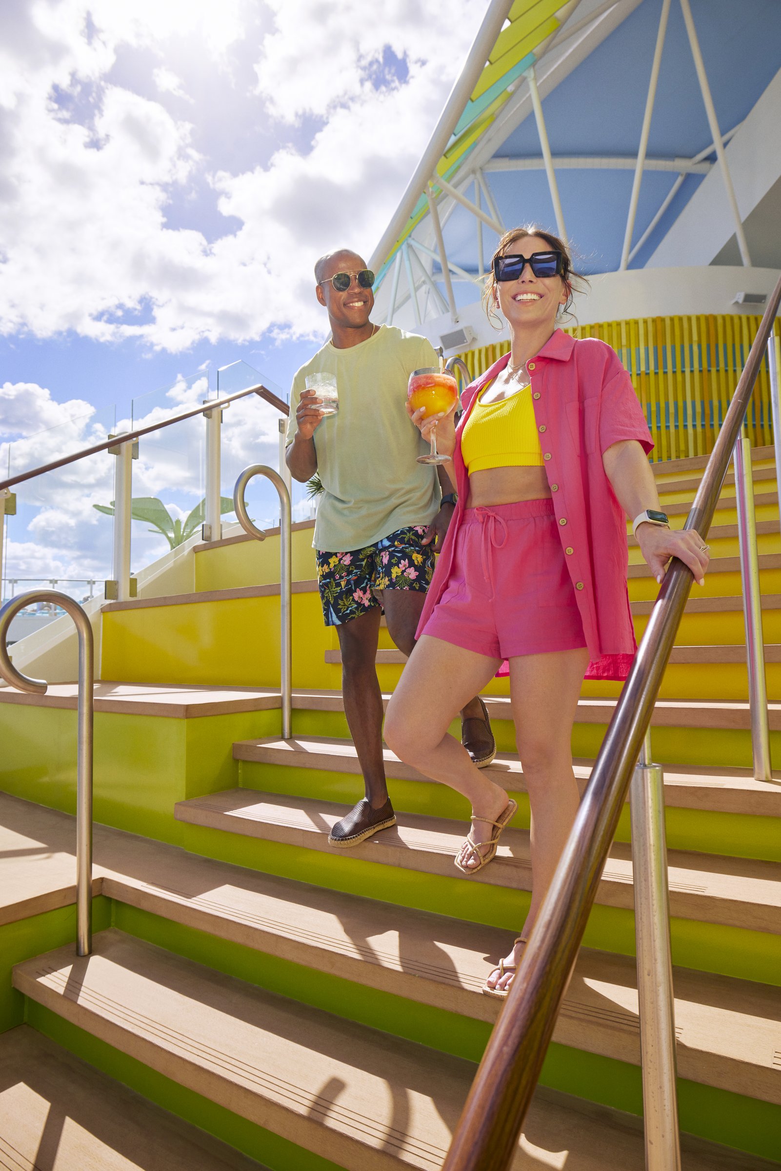 Couple with cocktails on sunlit steps at Lime & Coconut aboard Icon of the Seas