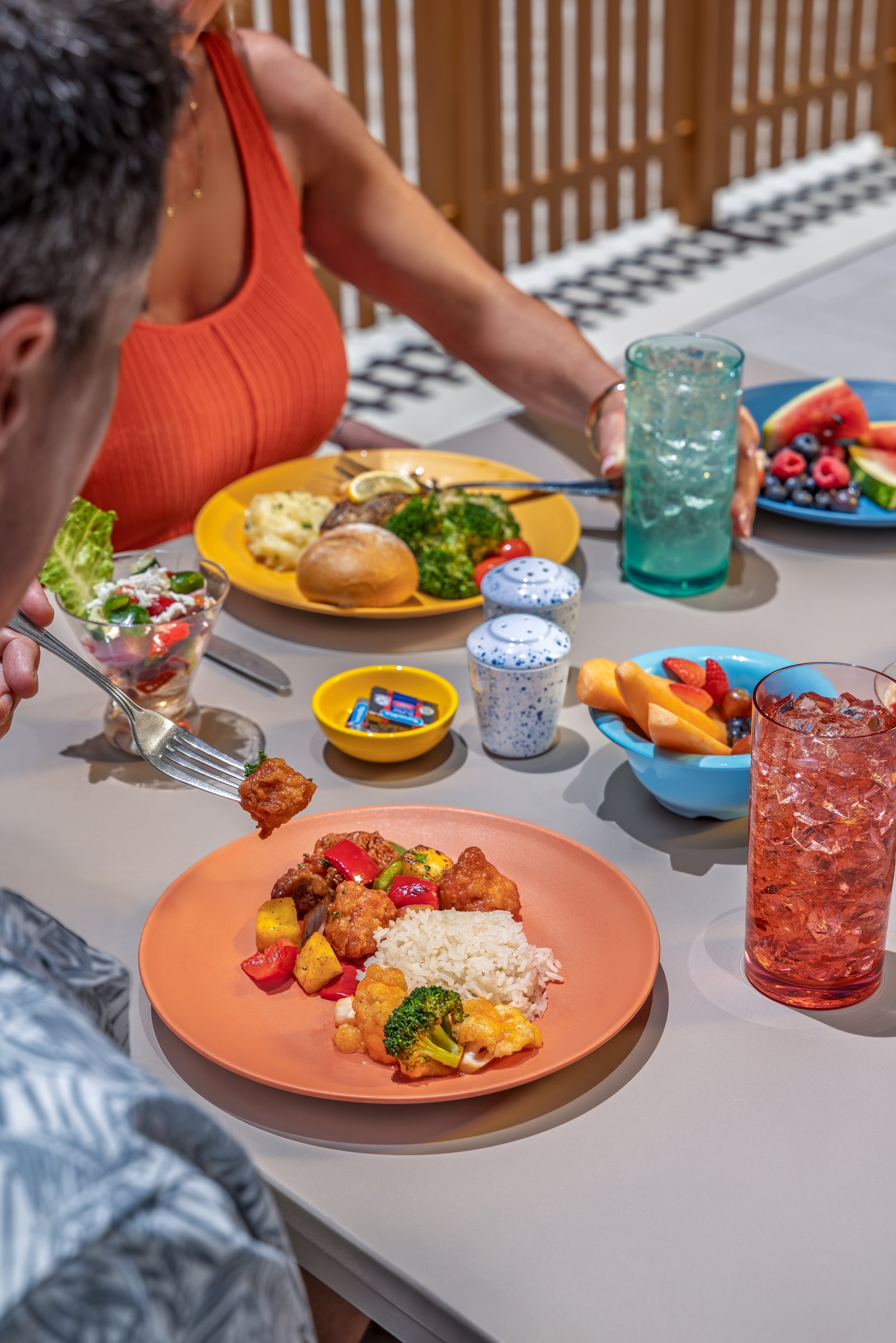 Sweet-and-sour pork, salad and fresh fruit on a sunny table at Surfside Eatery aboard Icon of the Seas