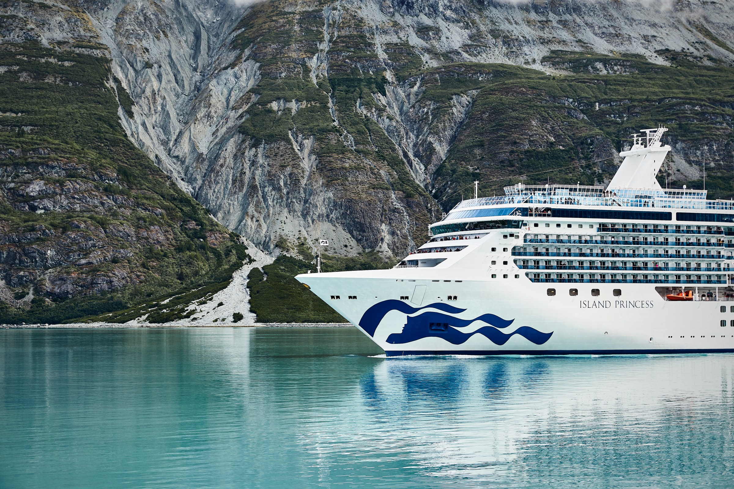 Island Princess bow sailing Alaska waters with steep mountains behind