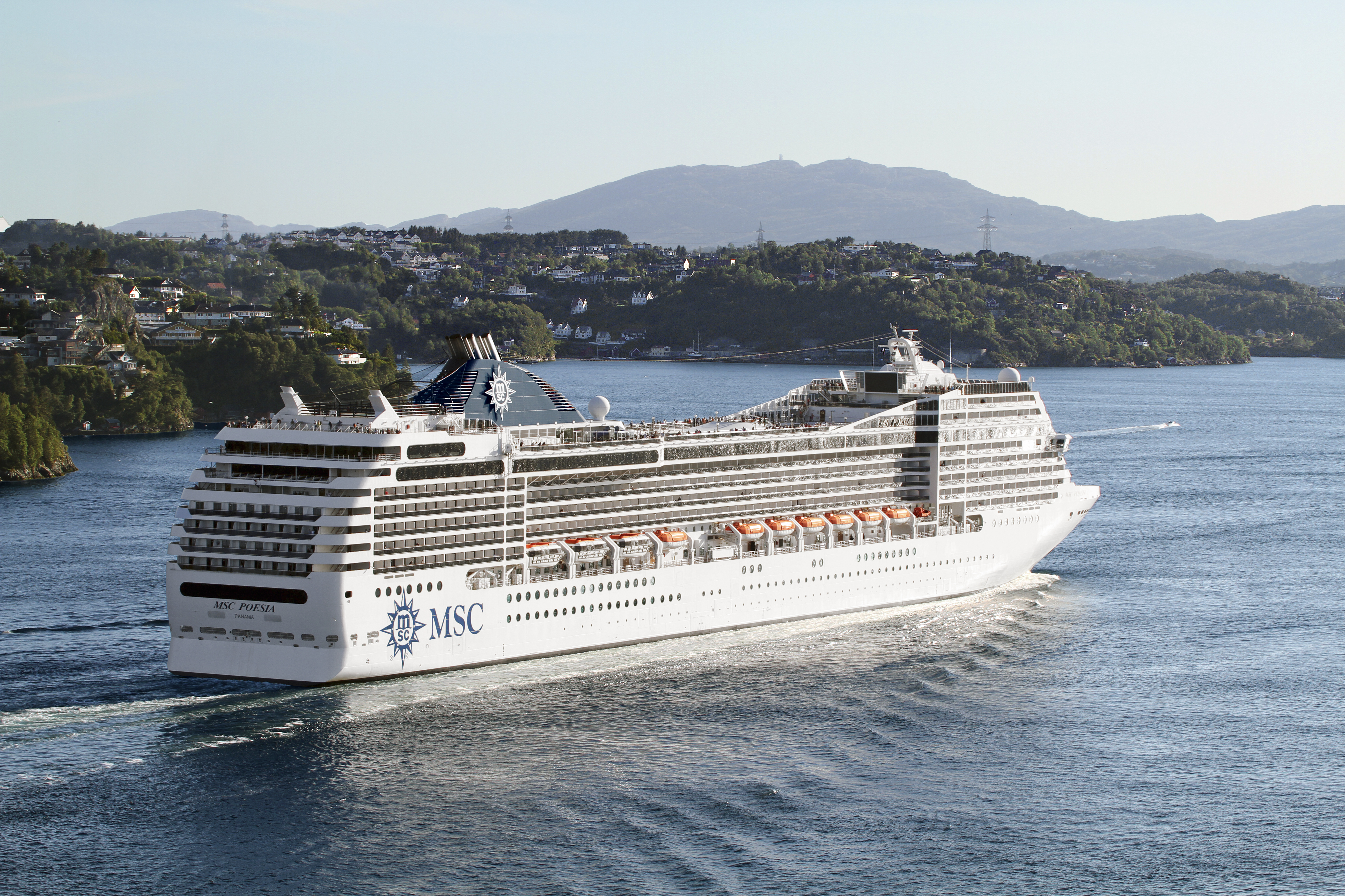 MSC Poesia sunny aerial stern exterior along a green coastal hillside