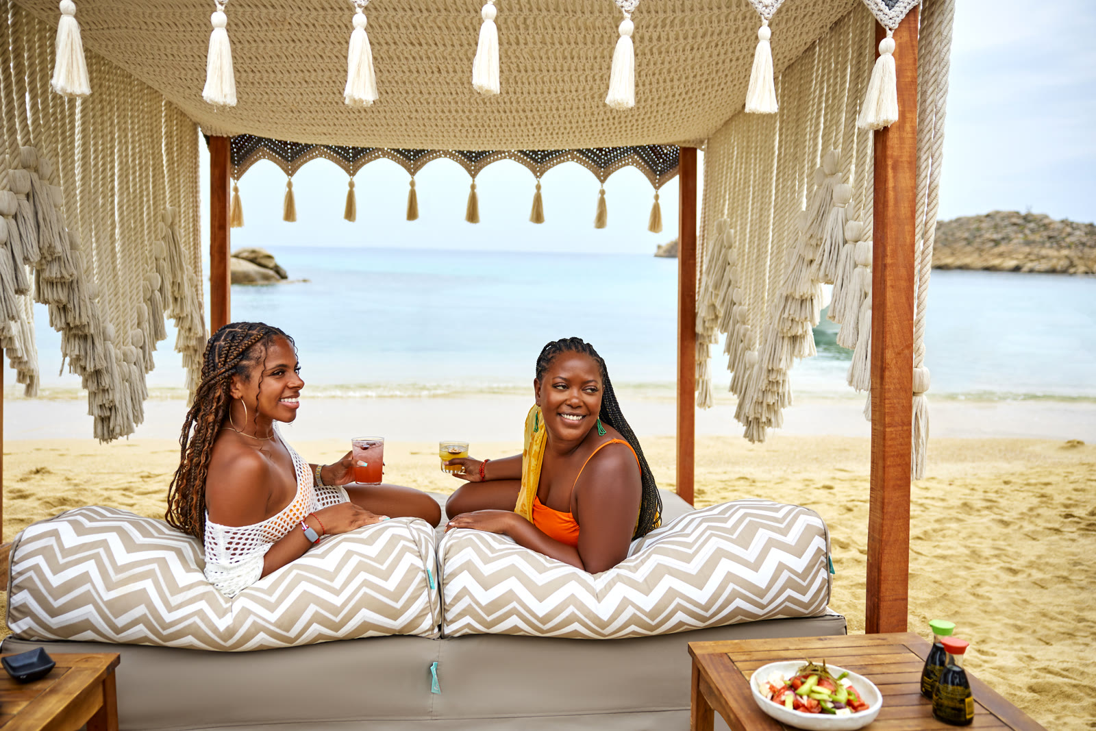 Two women relaxing at a Greek beach-club cabana.