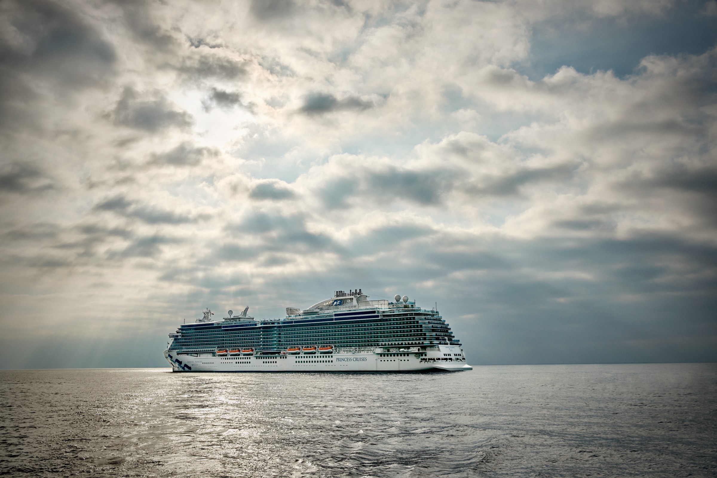 Royal Princess at sea under dramatic sunbeams through clouds