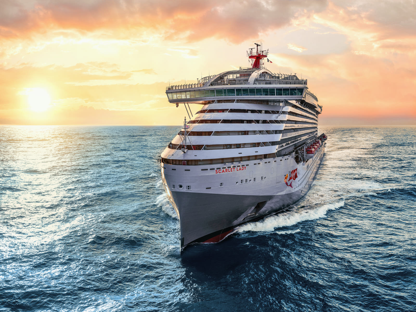 Scarlet Lady sailing toward the camera in open ocean under a golden sunset sky