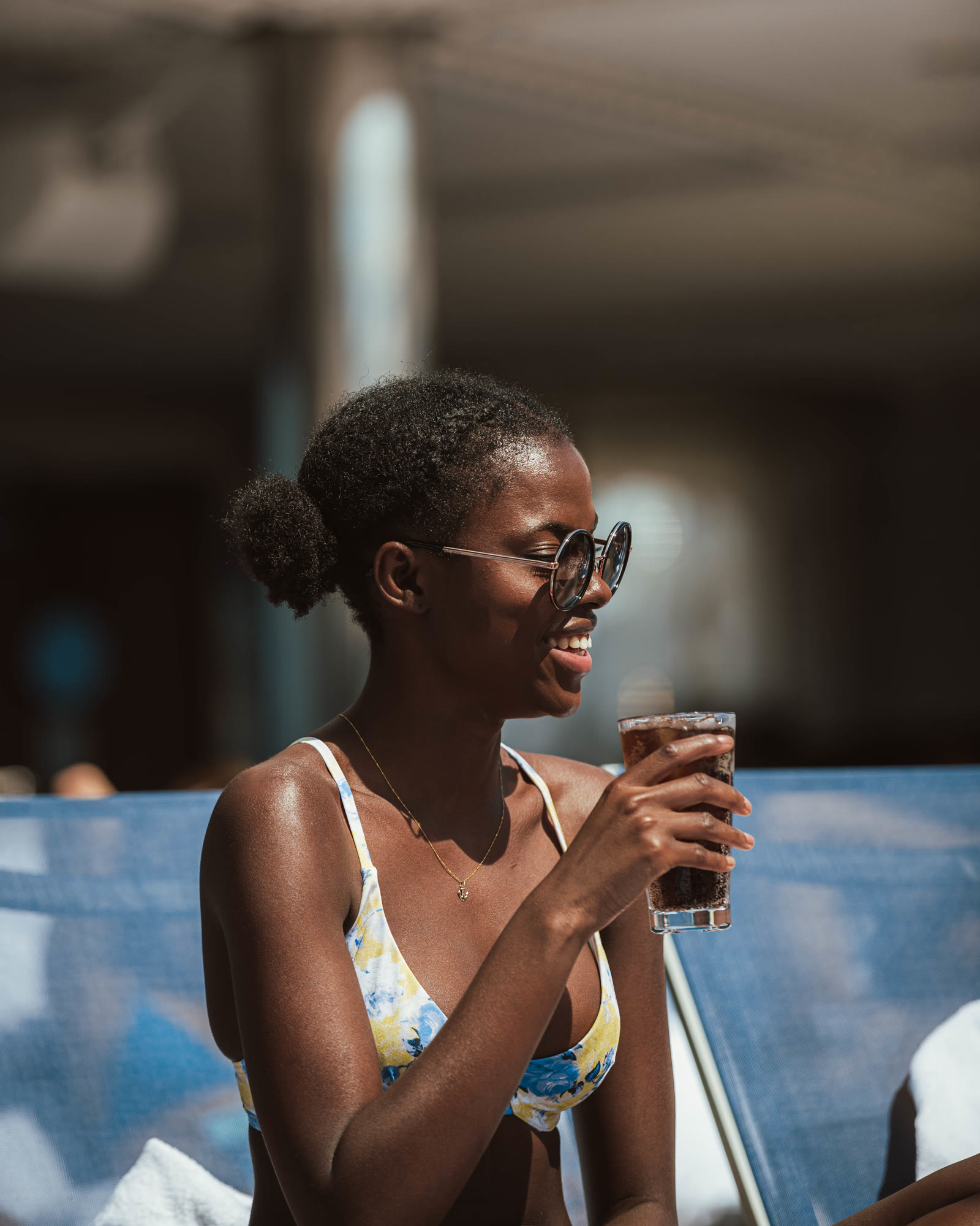 Woman wearing a bikini and sunglasses holding a drink poolside.