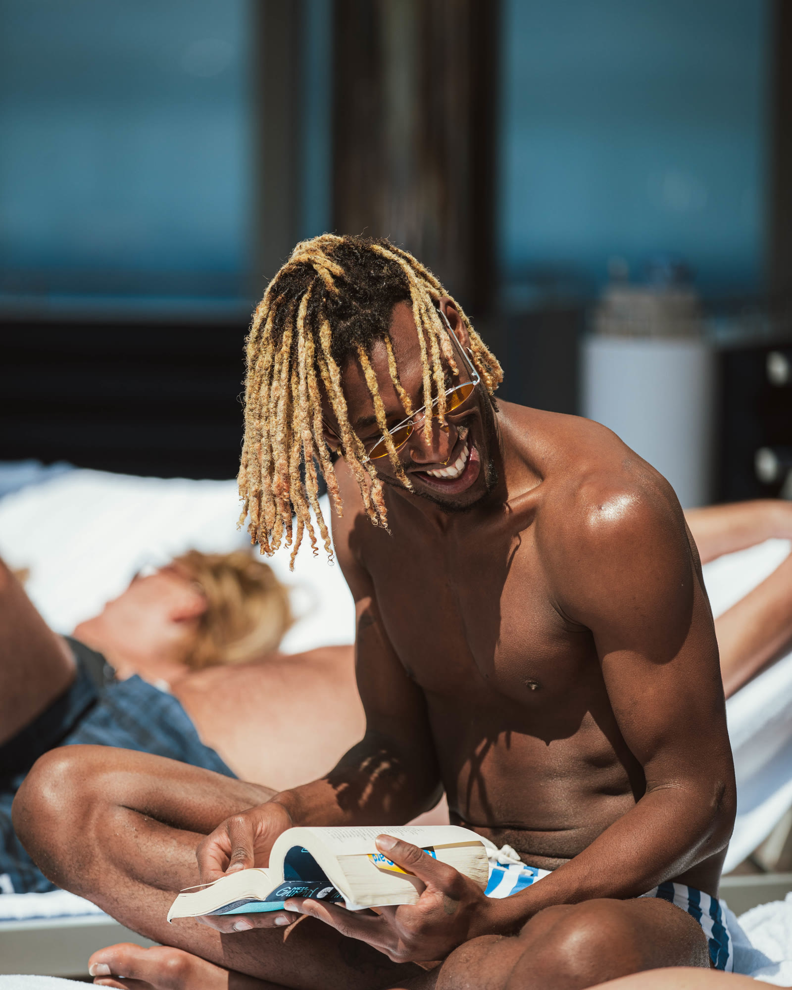 Man reading in the sun and smiling on a pool deck.