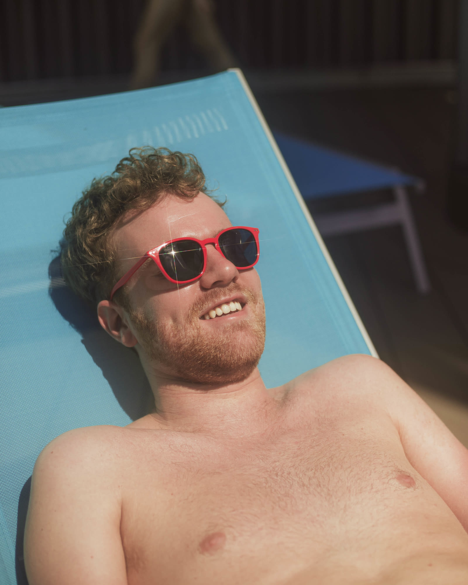 Man with red sunglasses sitting poolside.
