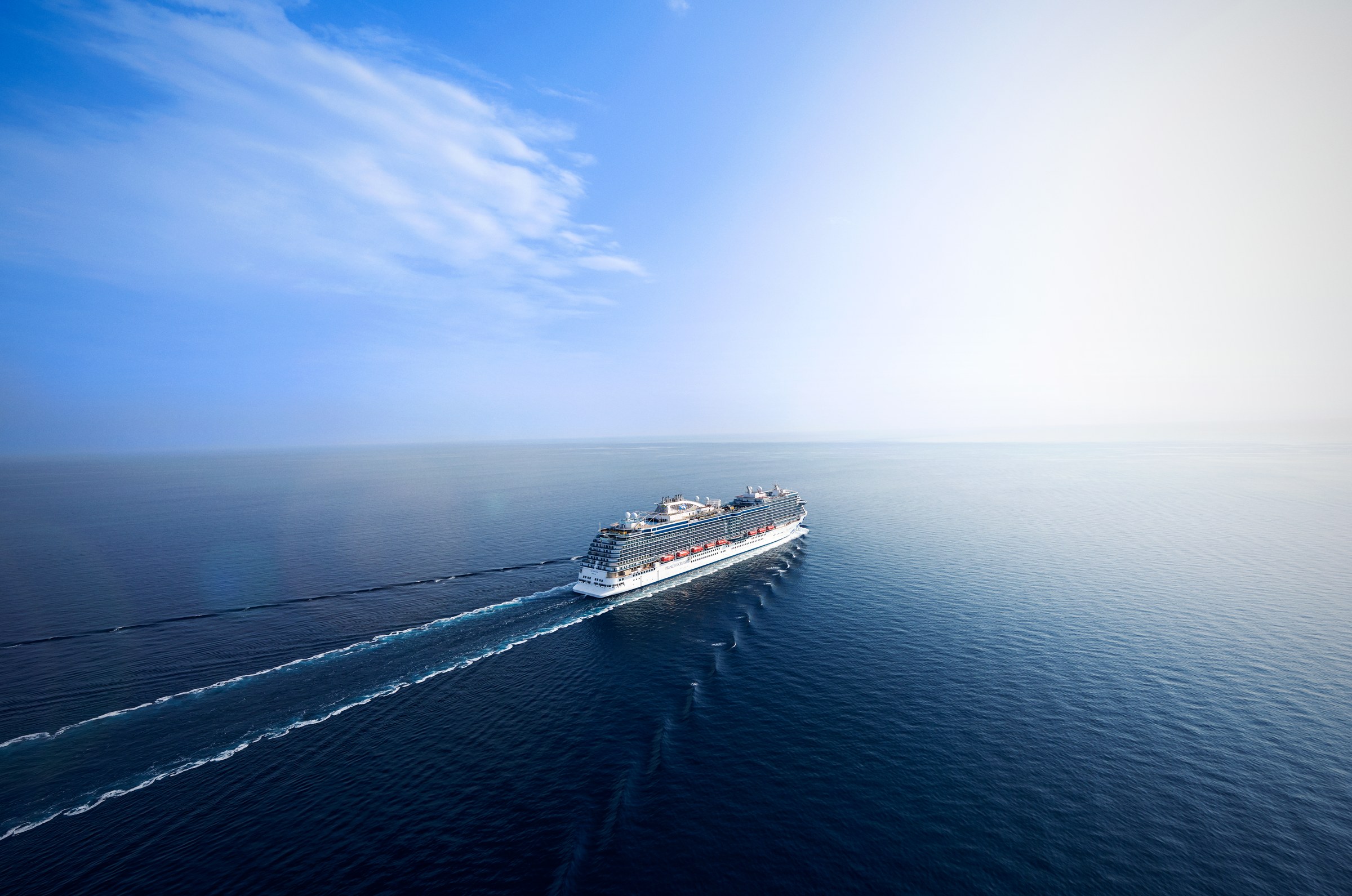 Aerial view of Sky Princess cruising a calm blue sea with a long wake