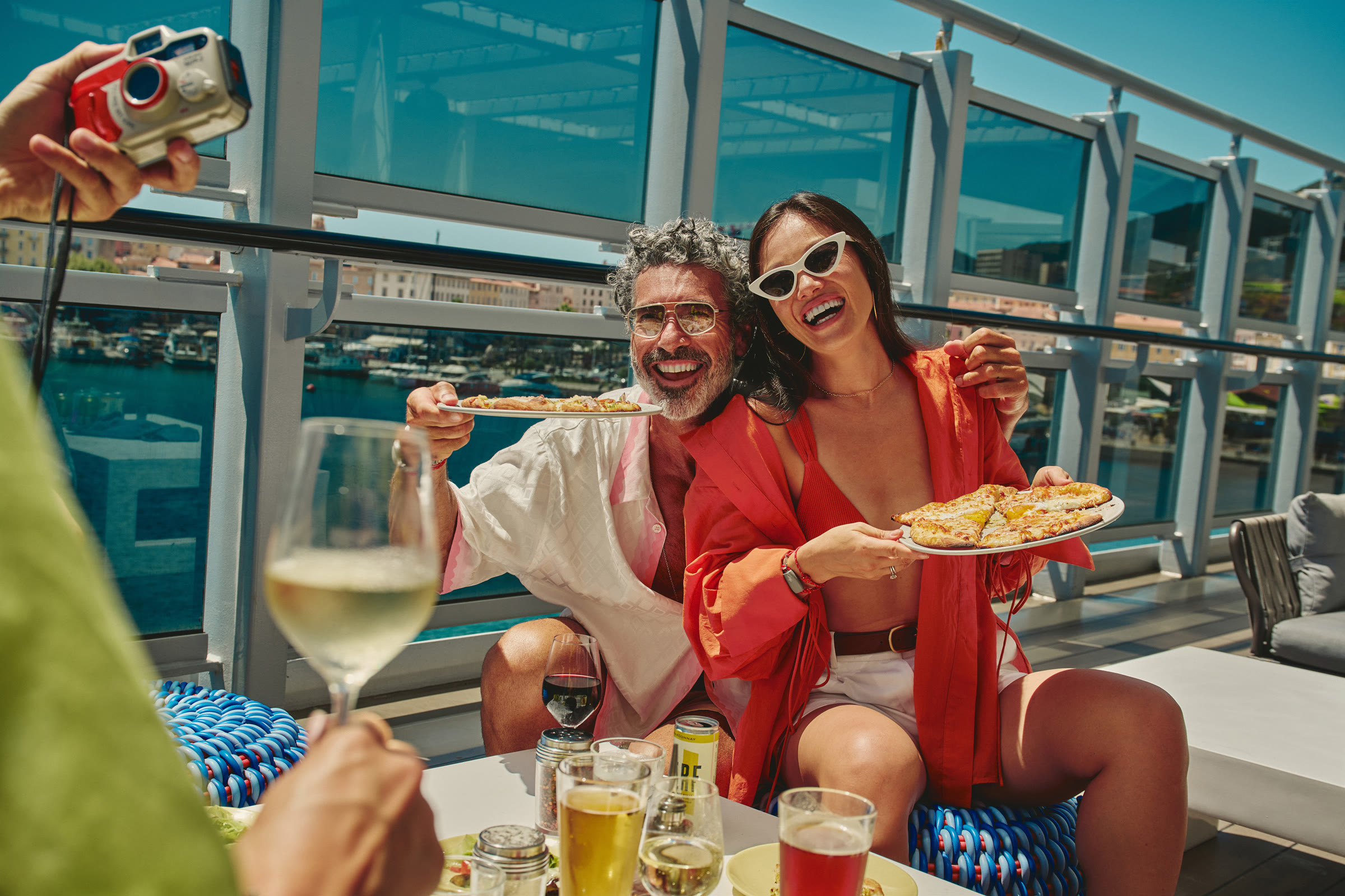 Sunny Pizza Place deck lunch with guests holding fresh pizza and drinks