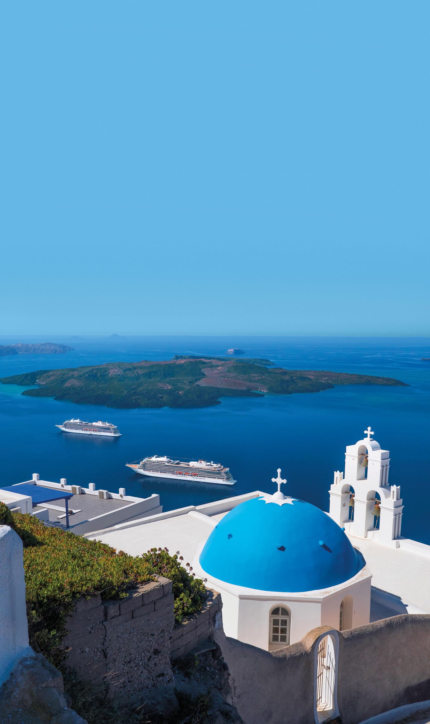 Viking Star and Viking Sea anchored in the Santorini caldera beyond a blue-domed church on a clear sunny day