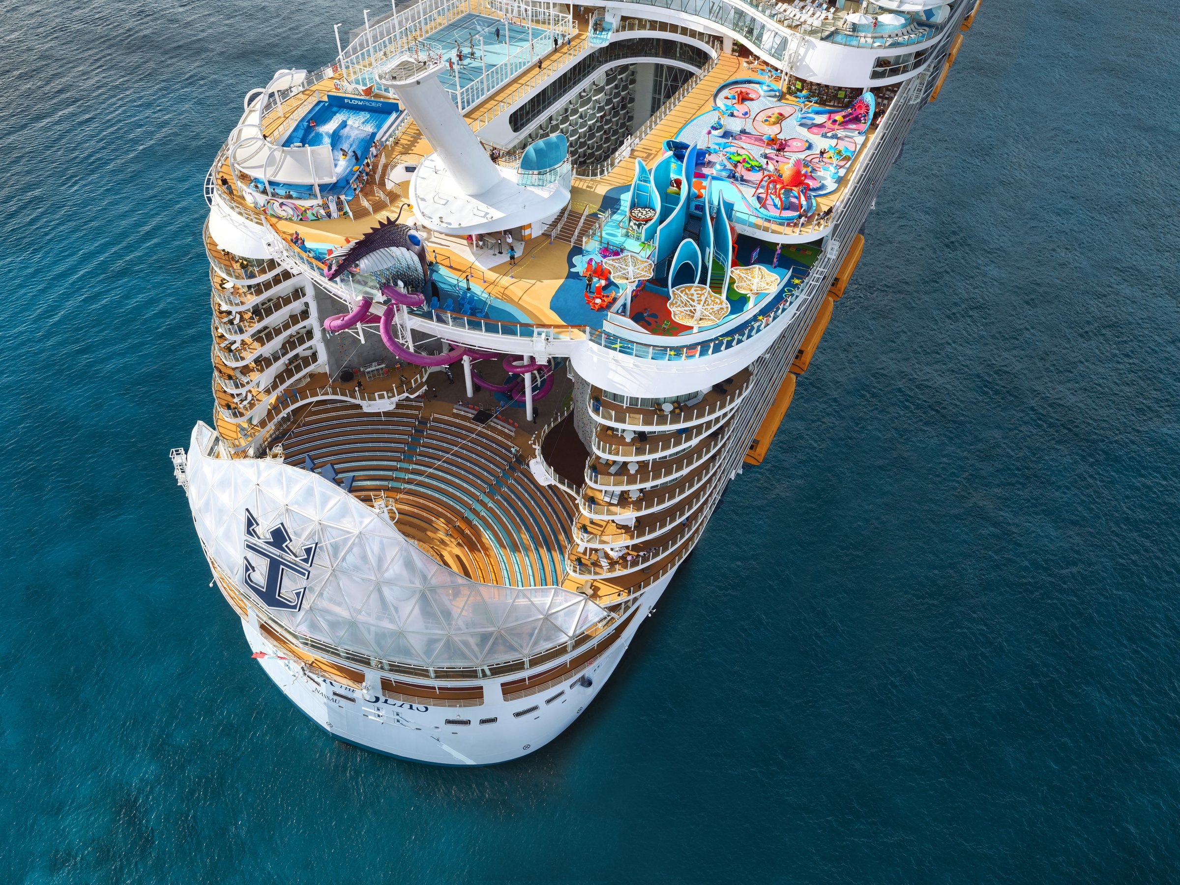Wonder of the Seas from the air on a bright day, looking forward over the stern, AquaTheater and top decks