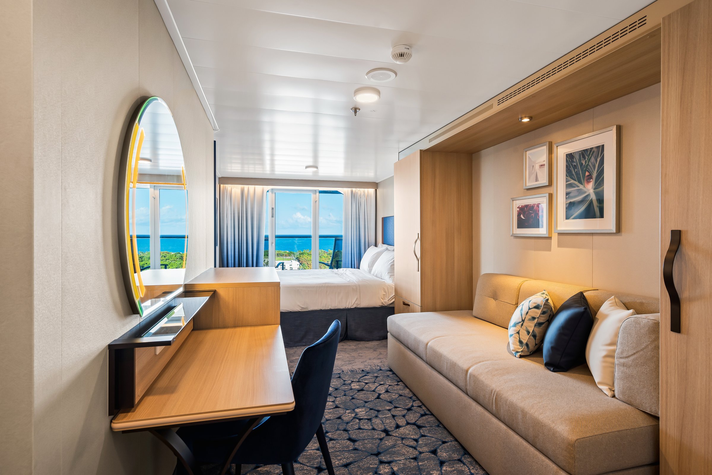 Connecting ocean view balcony stateroom aboard Wonder of the Seas with sofa, desk and sunny sea view