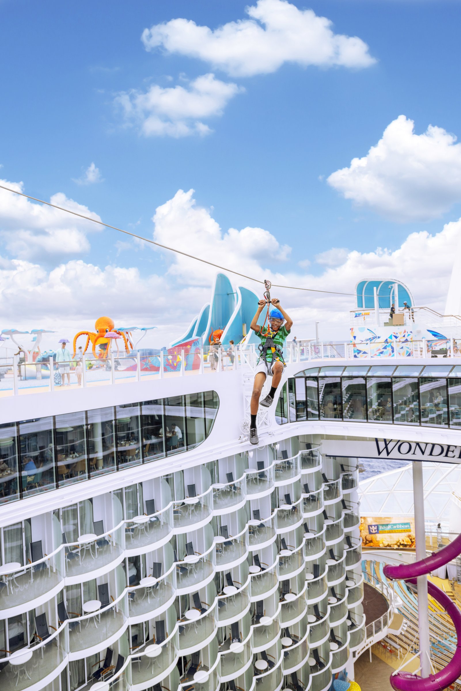 Rider on the zipline above the Boardwalk aboard Wonder of the Seas under a blue sky