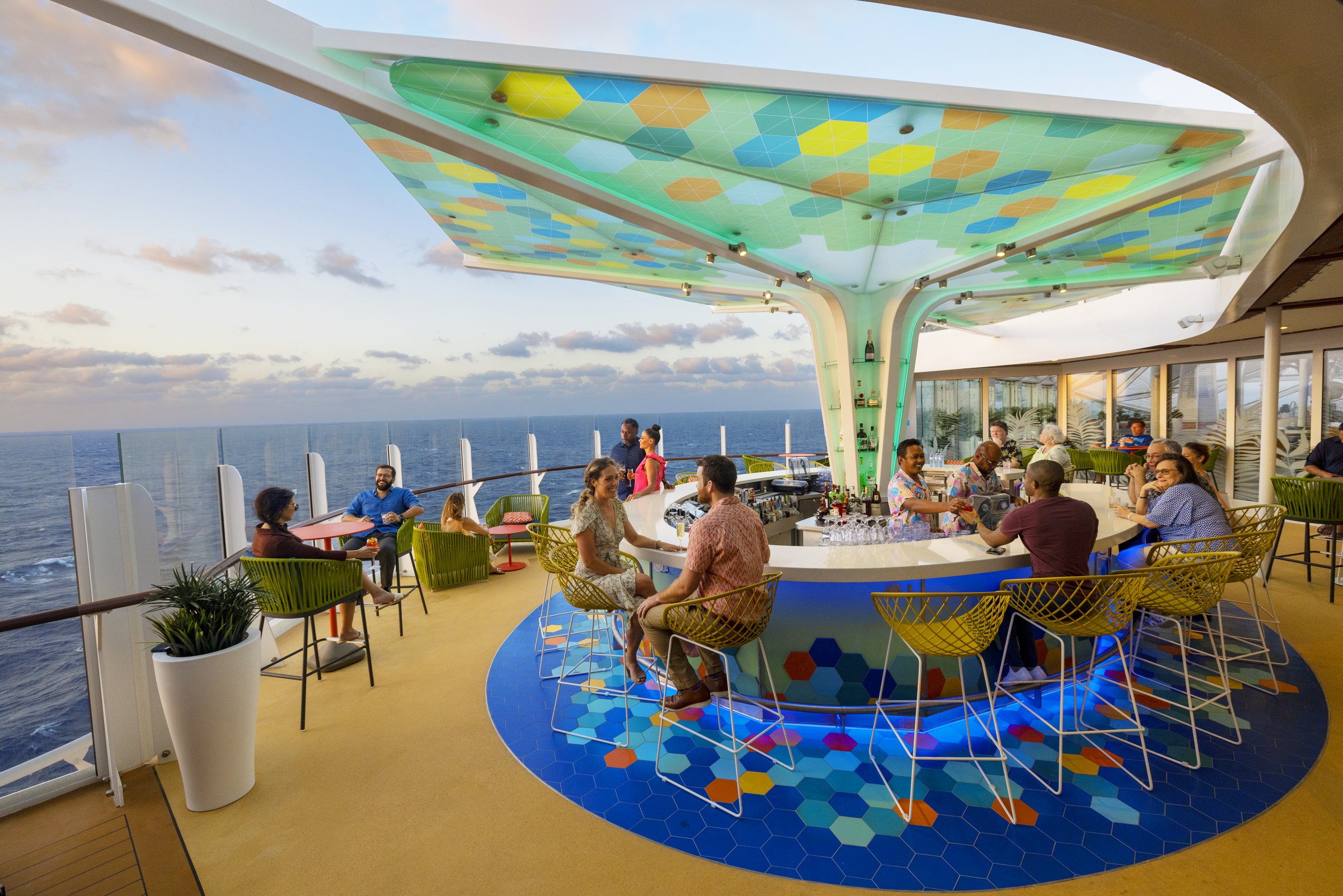 Guests at the open-air Vue Bar aboard Wonder of the Seas with ocean views in late-afternoon light